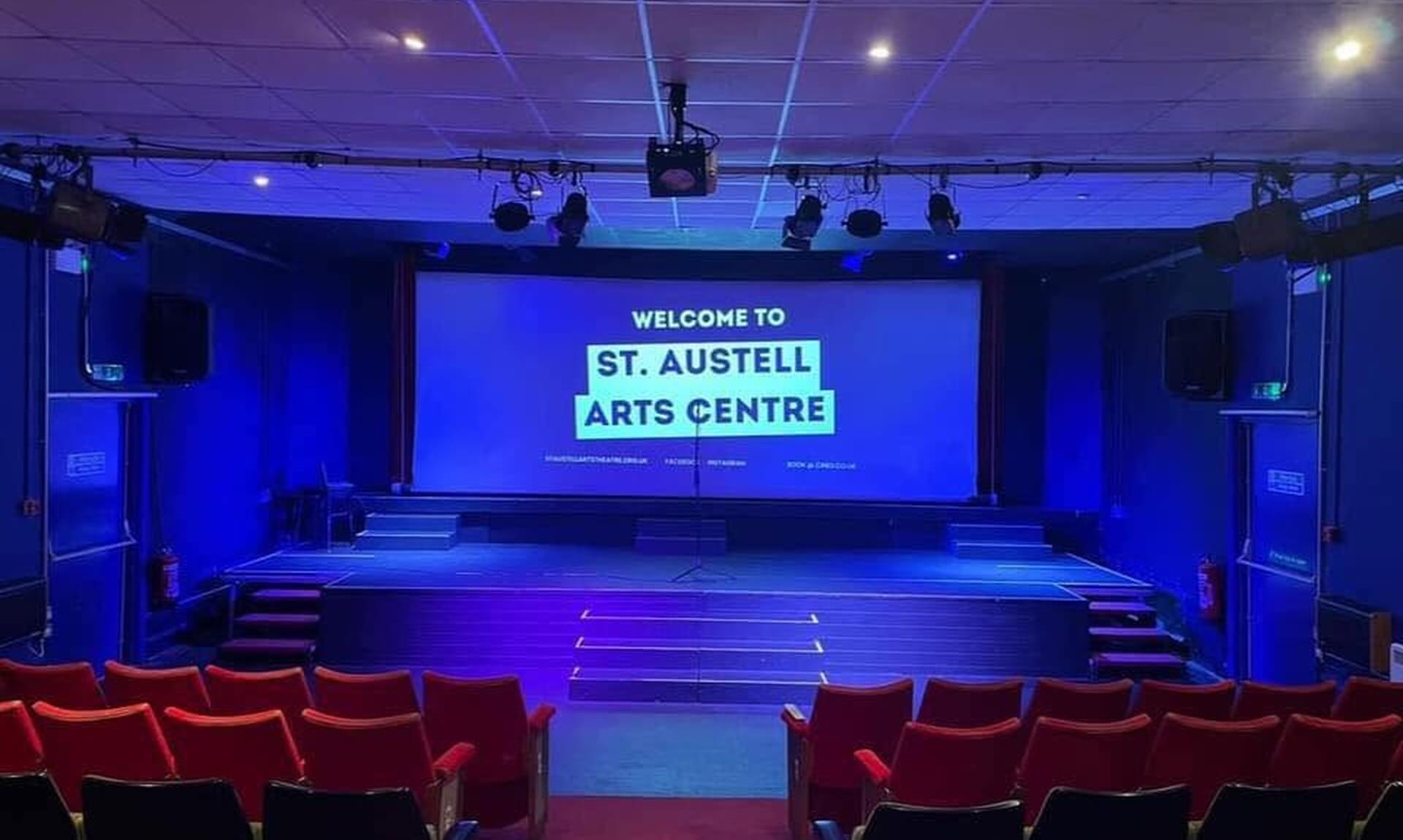 The auditorium and stage at St Austell Arts Centre with red seats and a welcome screen