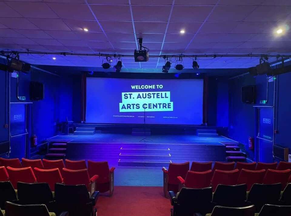 The auditorium and stage at St Austell Arts Centre with red seats and a welcome screen