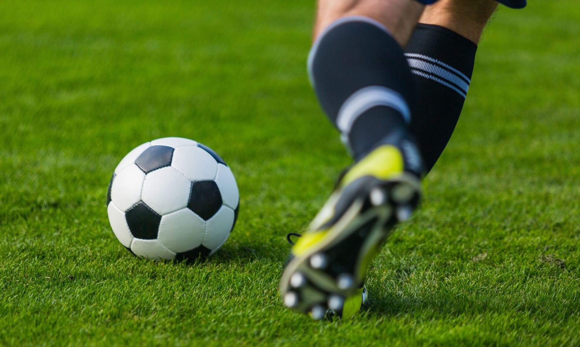Footballer's boot about to strike the ball on a grass pitch
