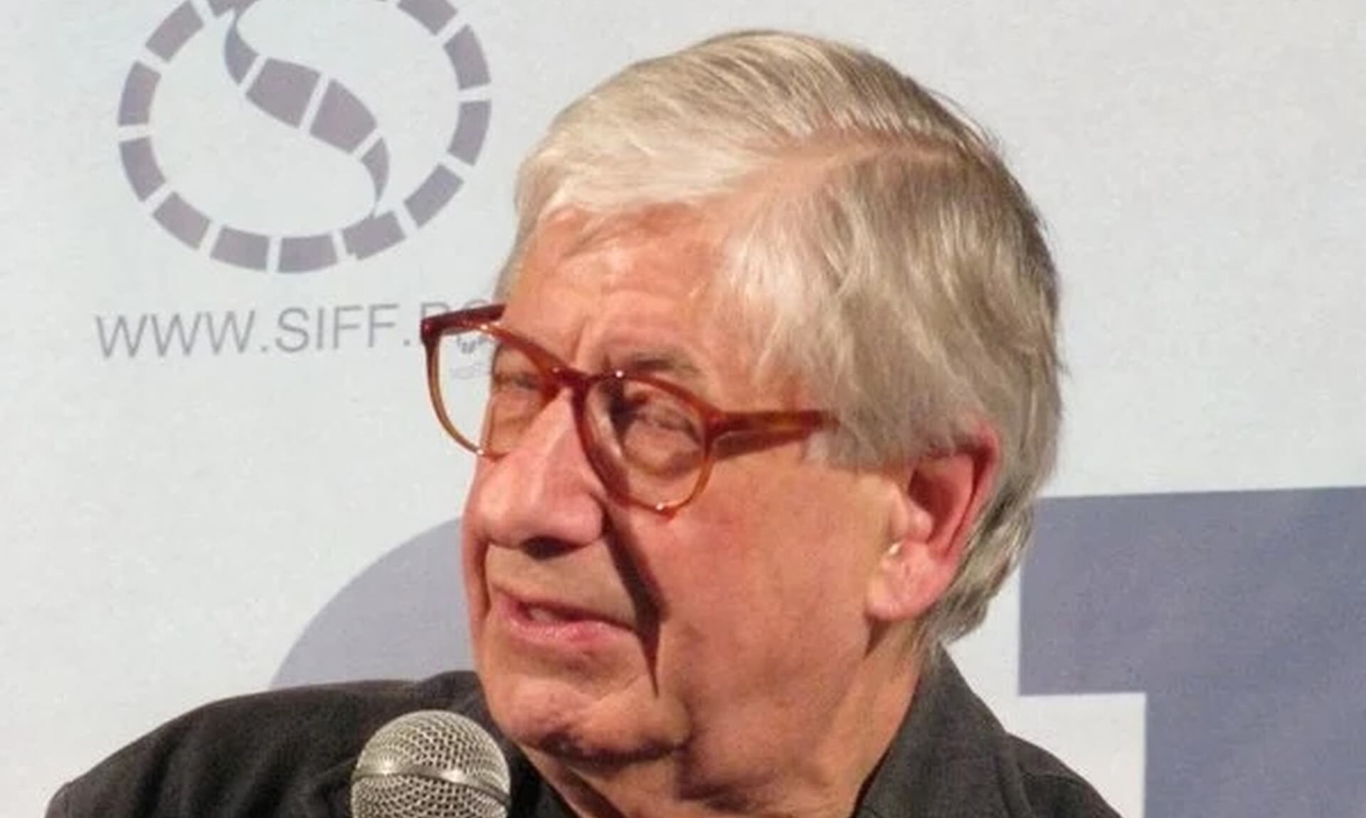 Tony Palmer speaking on stage holding a microphone
