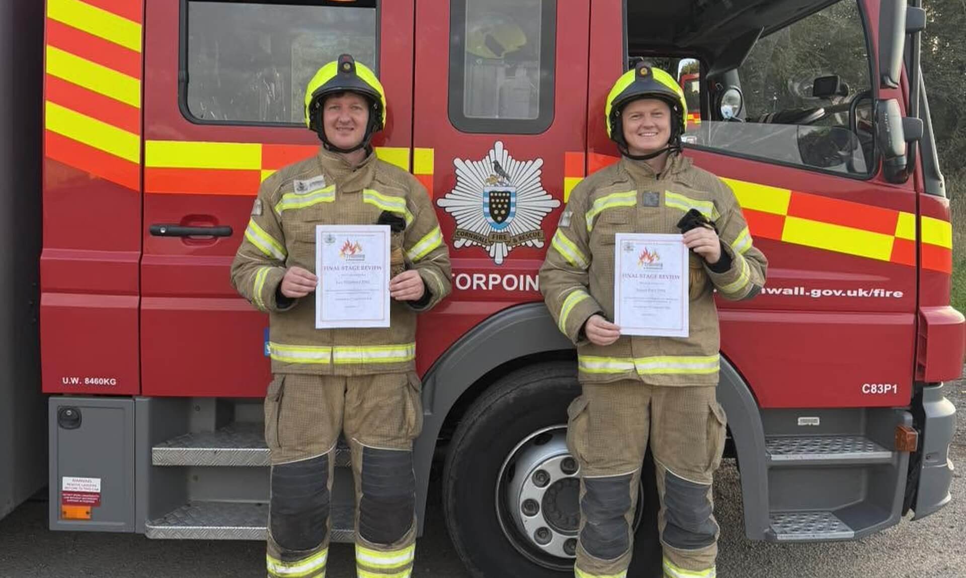 Firefighters Lee Shepherd and James Dart holding their final stage review certificates in front of a Torpoint fire engine