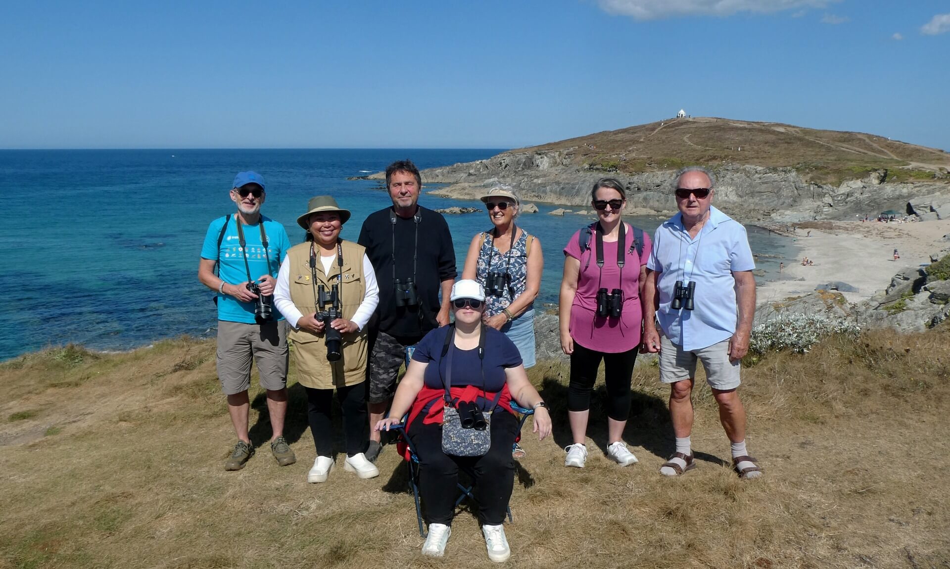 Birdwatching group on the clifftop at Towan Head, Newquay, with the headland and beach behind them