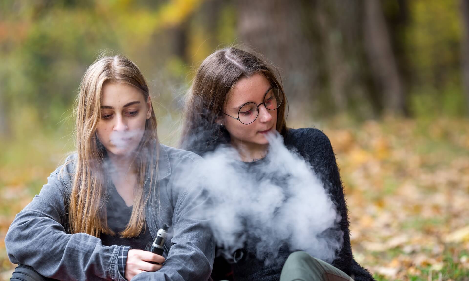 Two young women exhaling vape smoke outdoors
