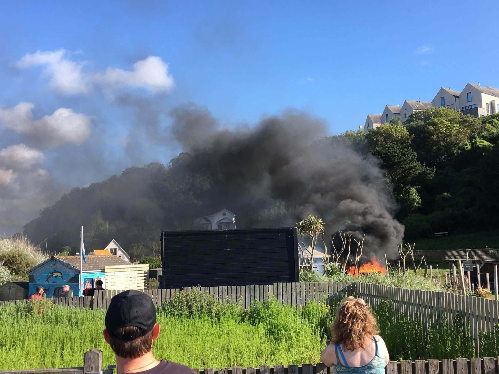 Black smoke rising from a beach fire watched by onlookers