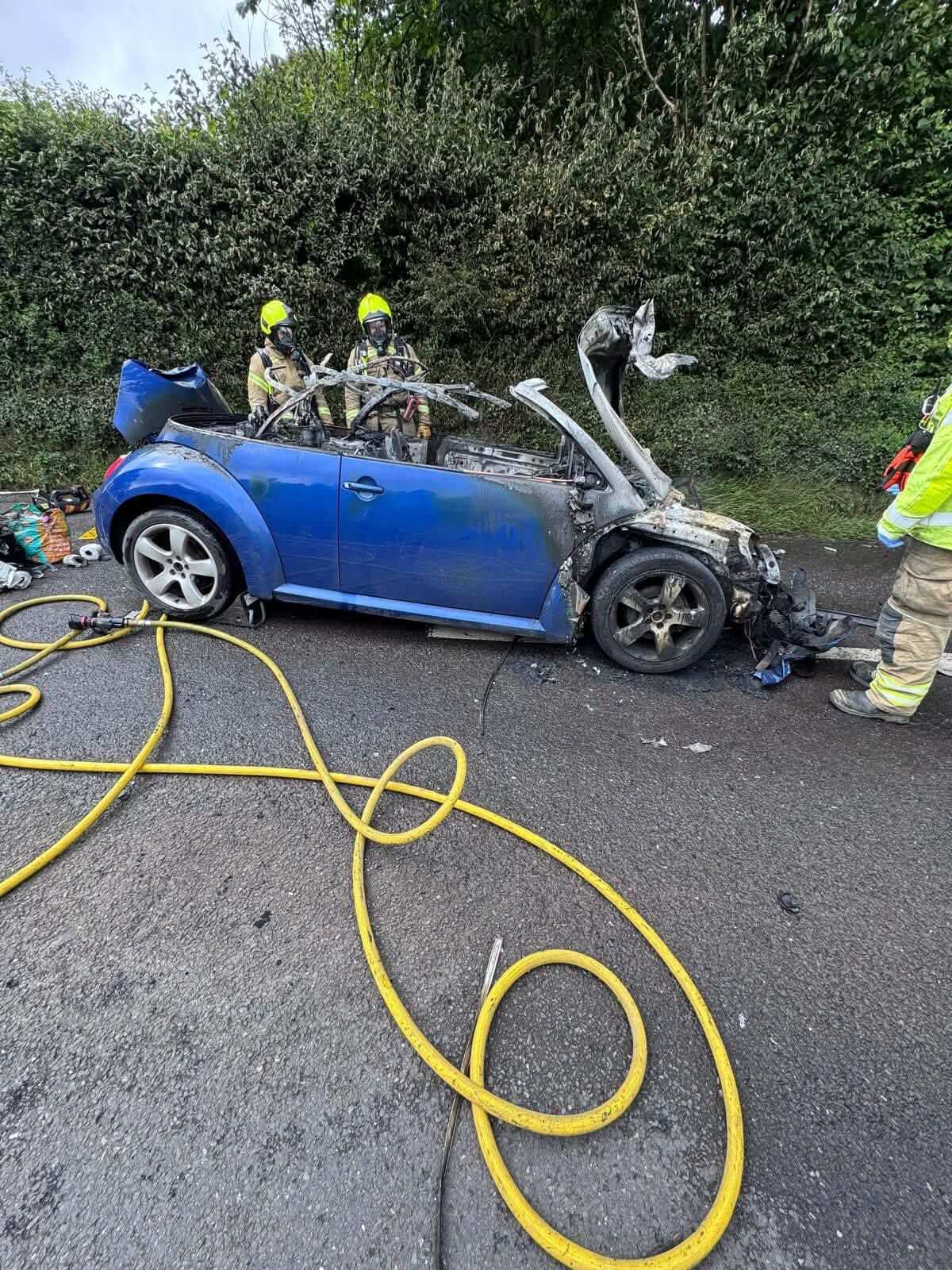 Firefighters in breathing apparatus at a burnt-out convertible car