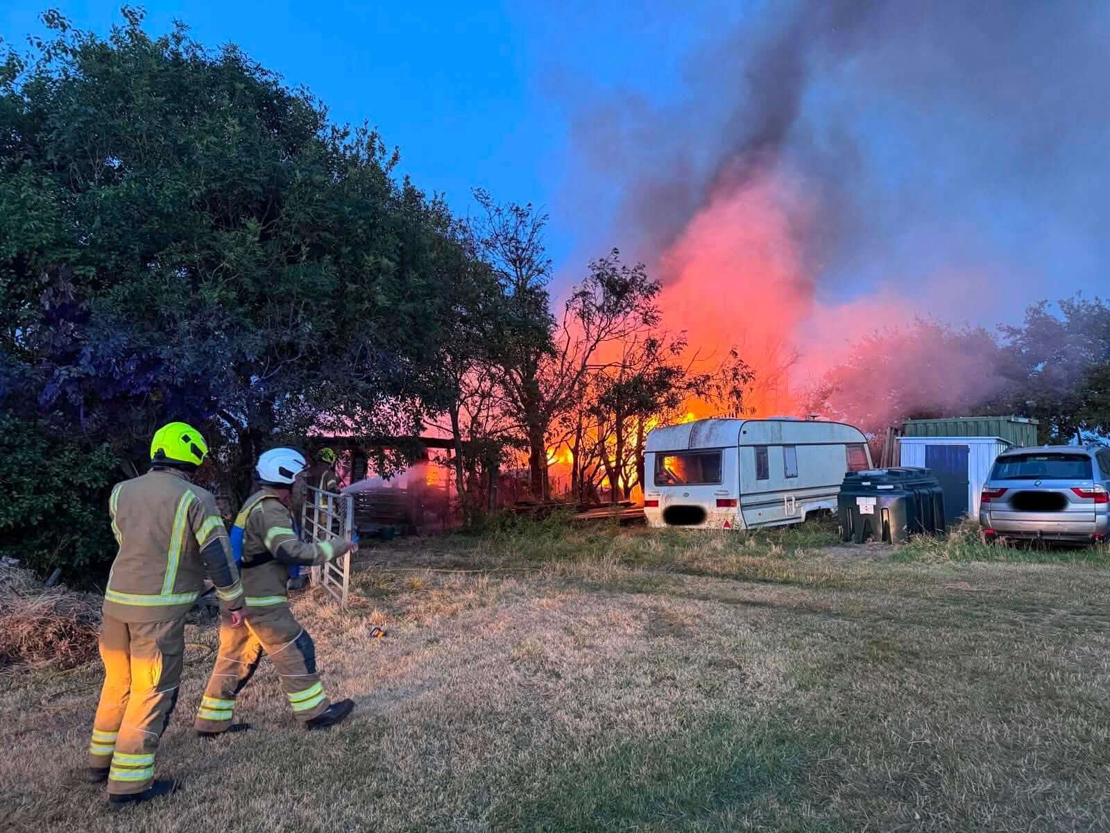 Caravan alight at dusk with firefighters approaching