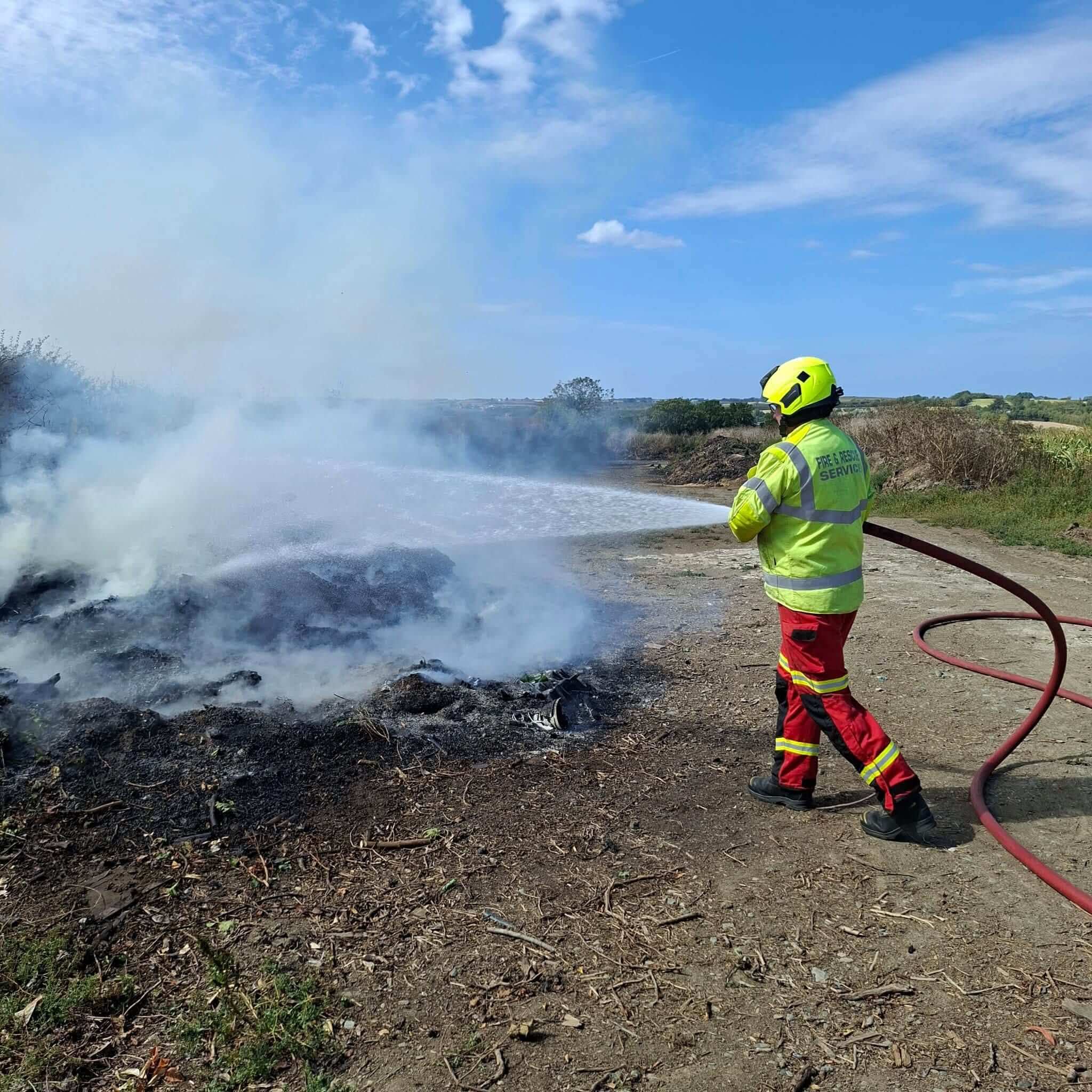 Firefighter hosing down a smouldering rubbish fire