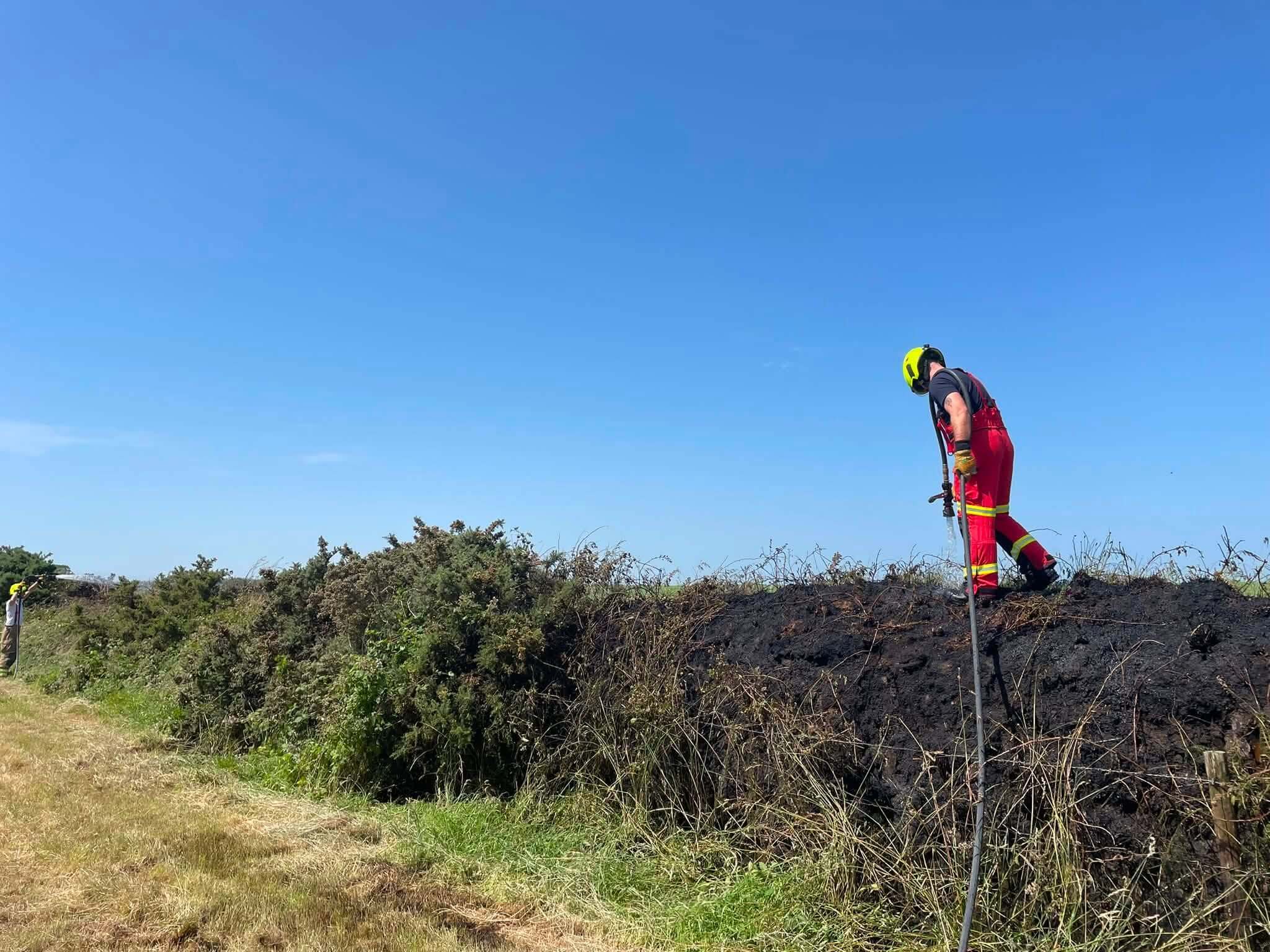 Firefighter damping down a gorse fire under blue skies