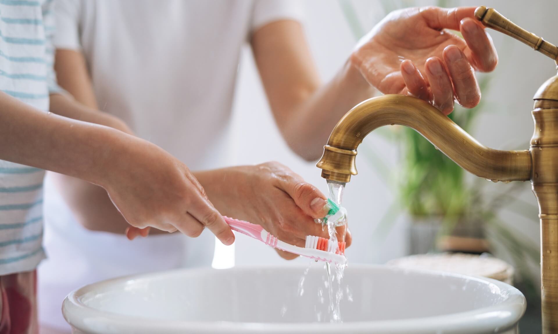 A parent and child washing hands and a toothbrush under a running tap