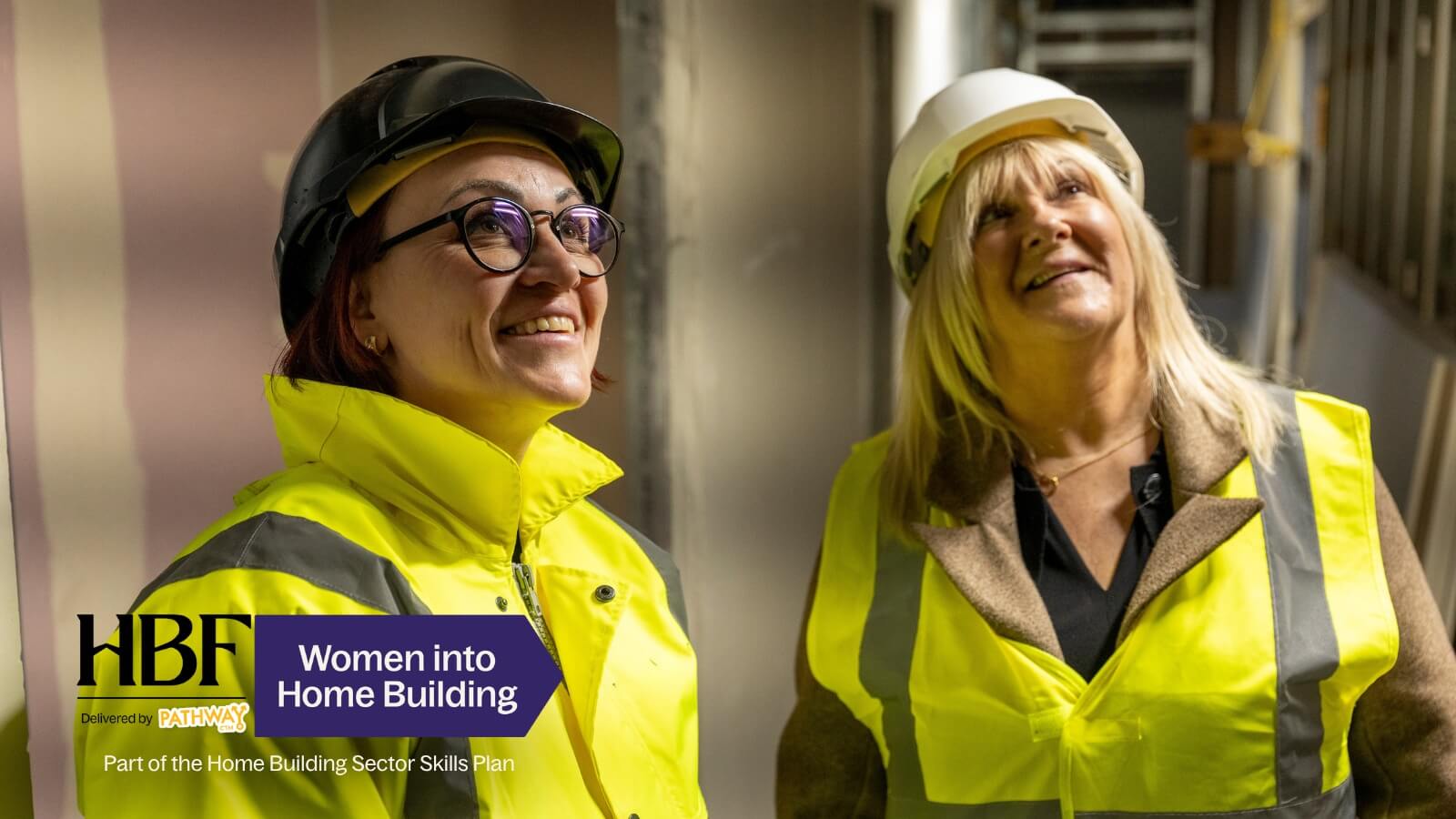 Two women in hard hats on a site tour looking up at construction work