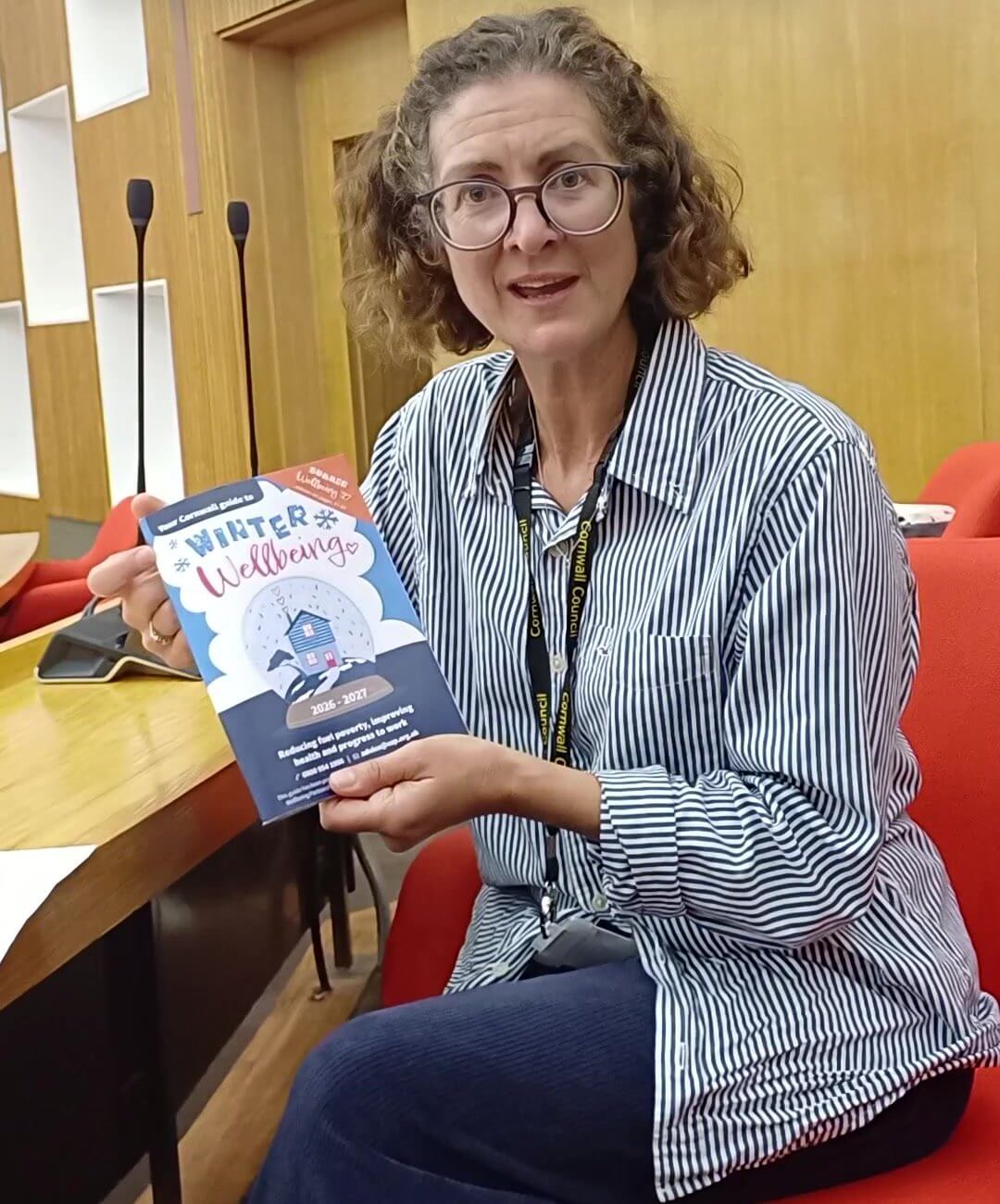 A woman holding a copy of the 2026/27 Winter Wellbeing Guide for Cornwall