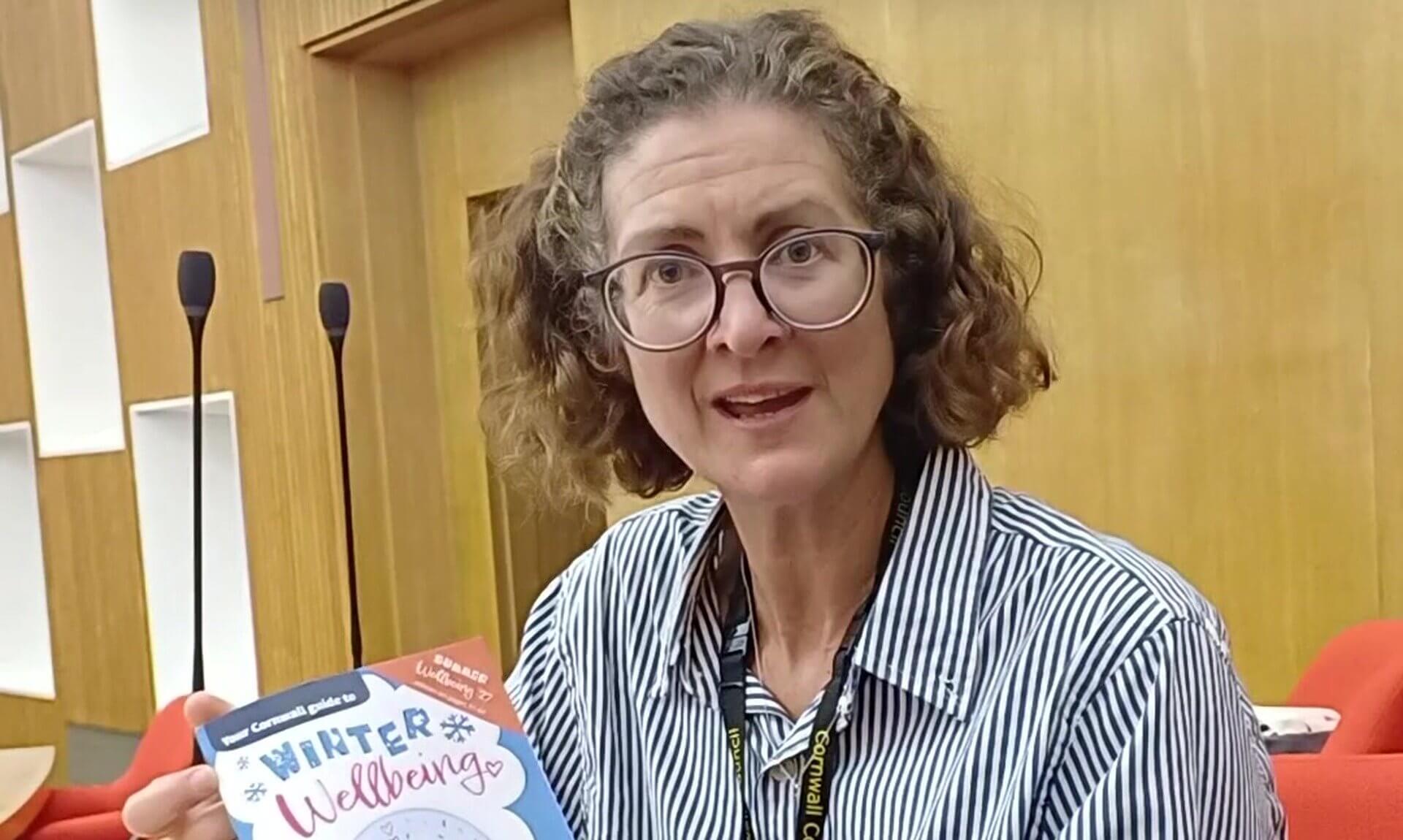 A woman holding a copy of the 2026/27 Winter Wellbeing Guide for Cornwall