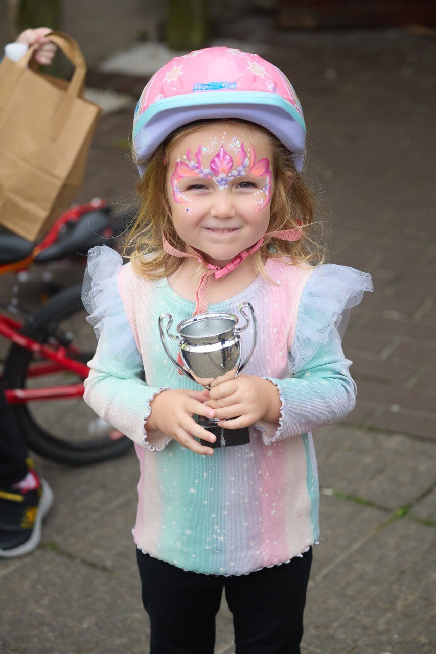 A young girl in face paint holding her Tykes on Trikes trophy