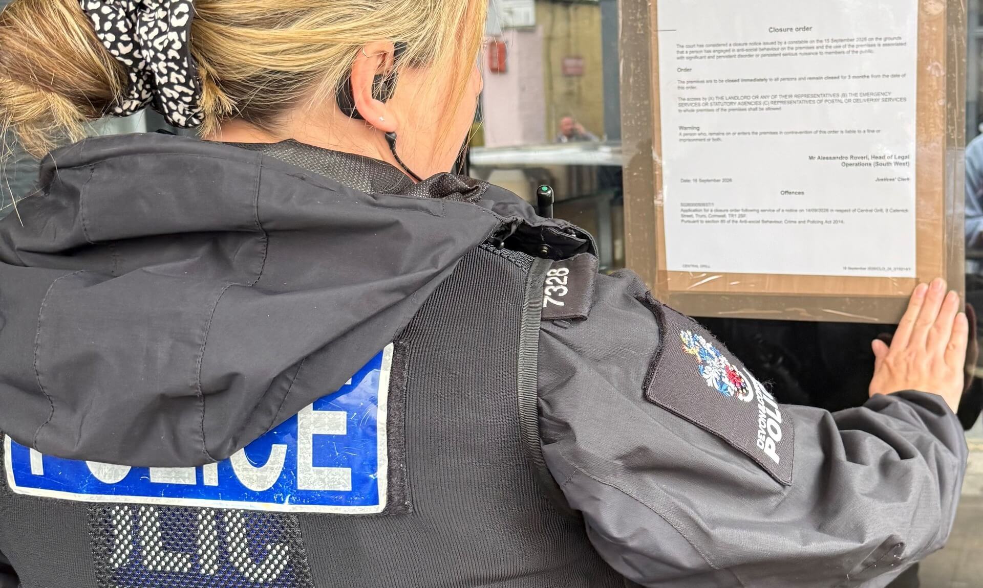 Police officer posting a closure order notice on the window of Central Grill in Truro