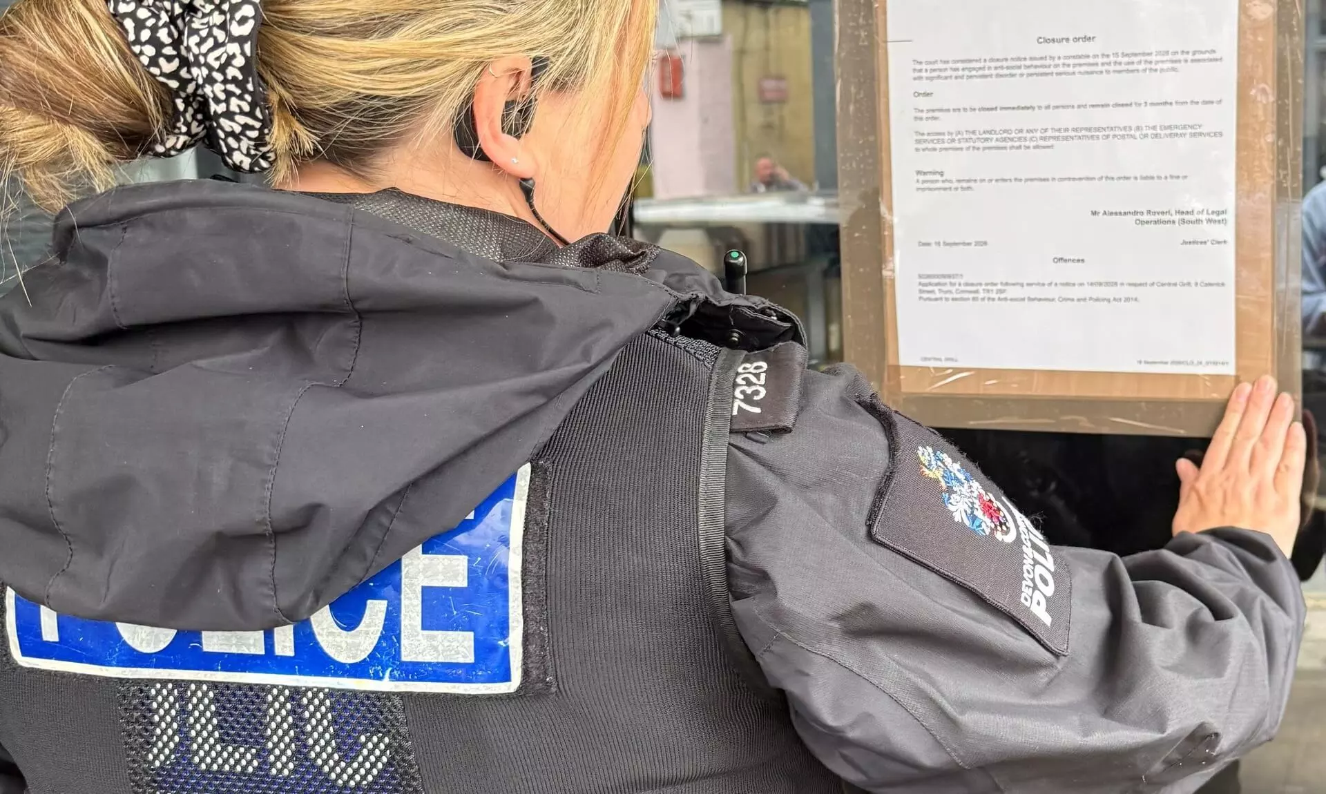 Police officer posting a closure order notice on the window of Central Grill in Truro