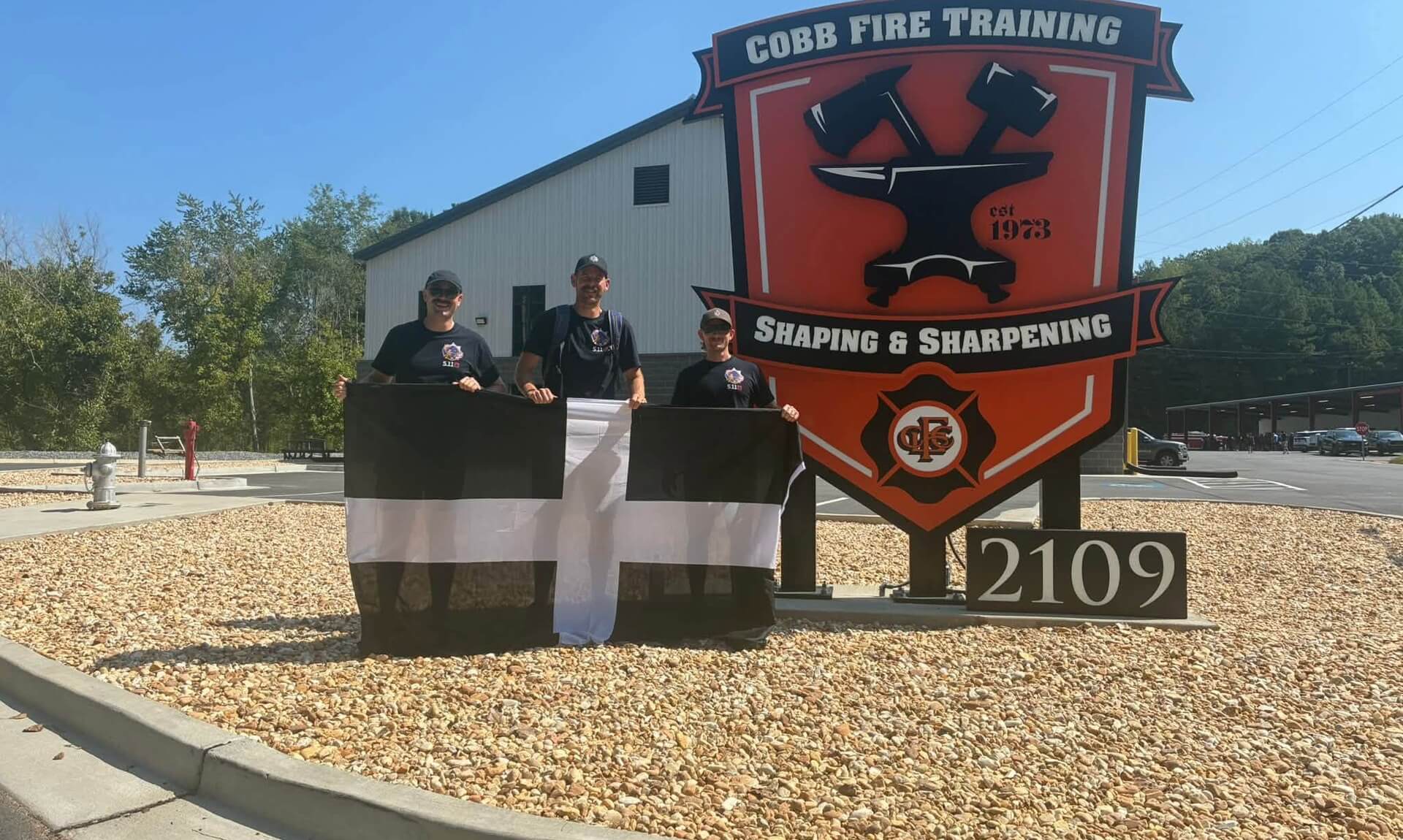 Three Cornwall firefighters holding a Cornish flag in front of the Cobb Fire Training sign in Atlanta