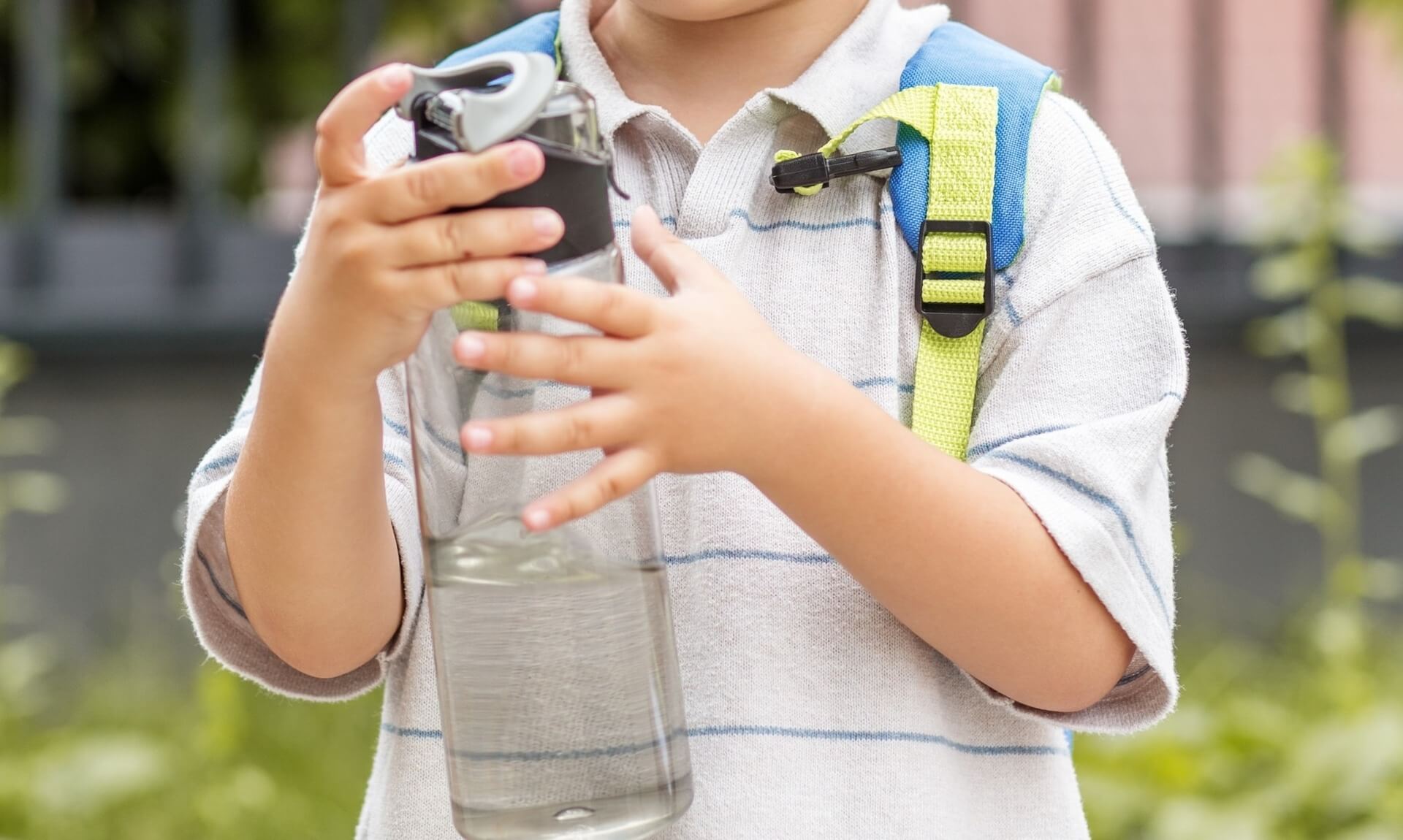 A child holding a water bottle while wearing a school backpack