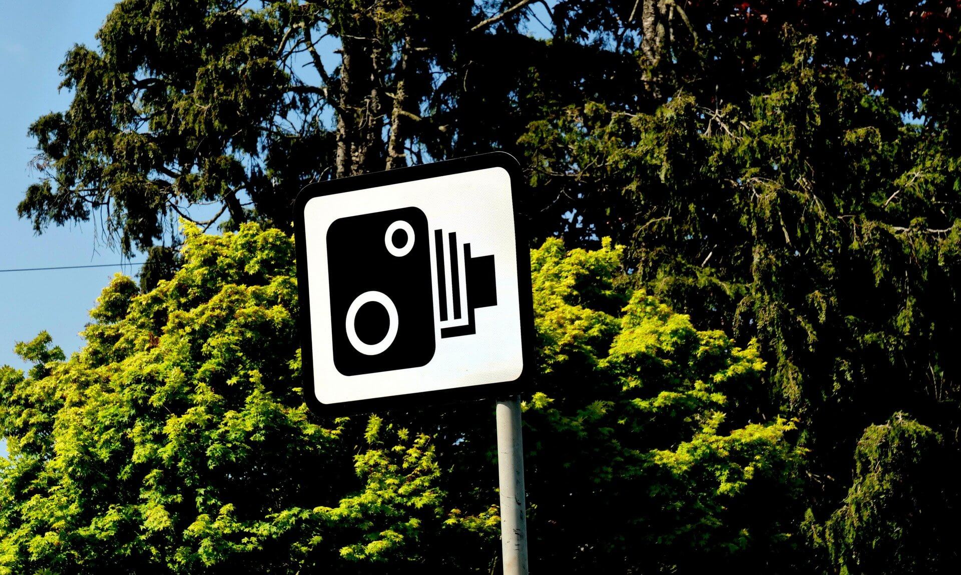Speed camera warning sign in front of trees