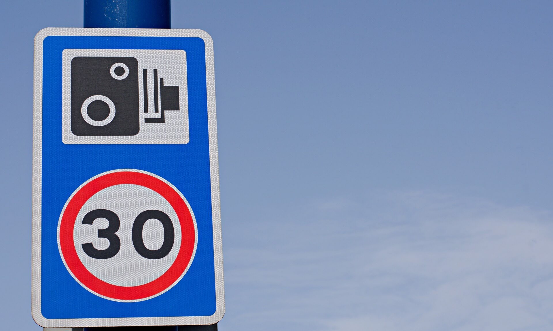 A speed camera warning sign with a 30mph limit roundel against a blue sky