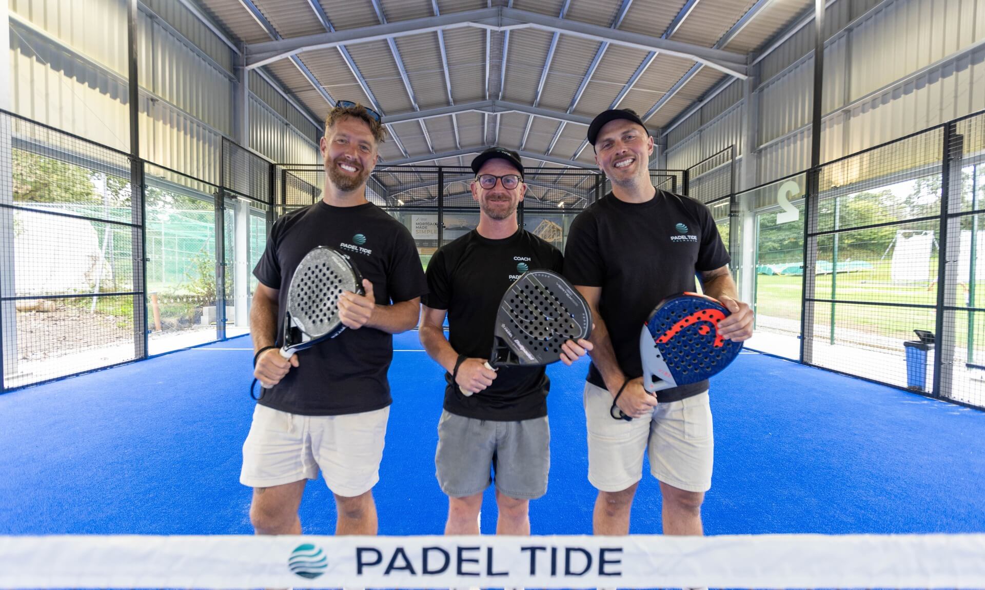 Padel Tide founders holding padel rackets on the new covered court at Falmouth Cricket Club