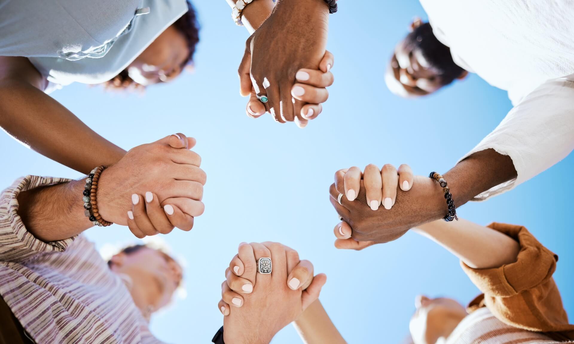 A circle of hands clasped together against a blue sky