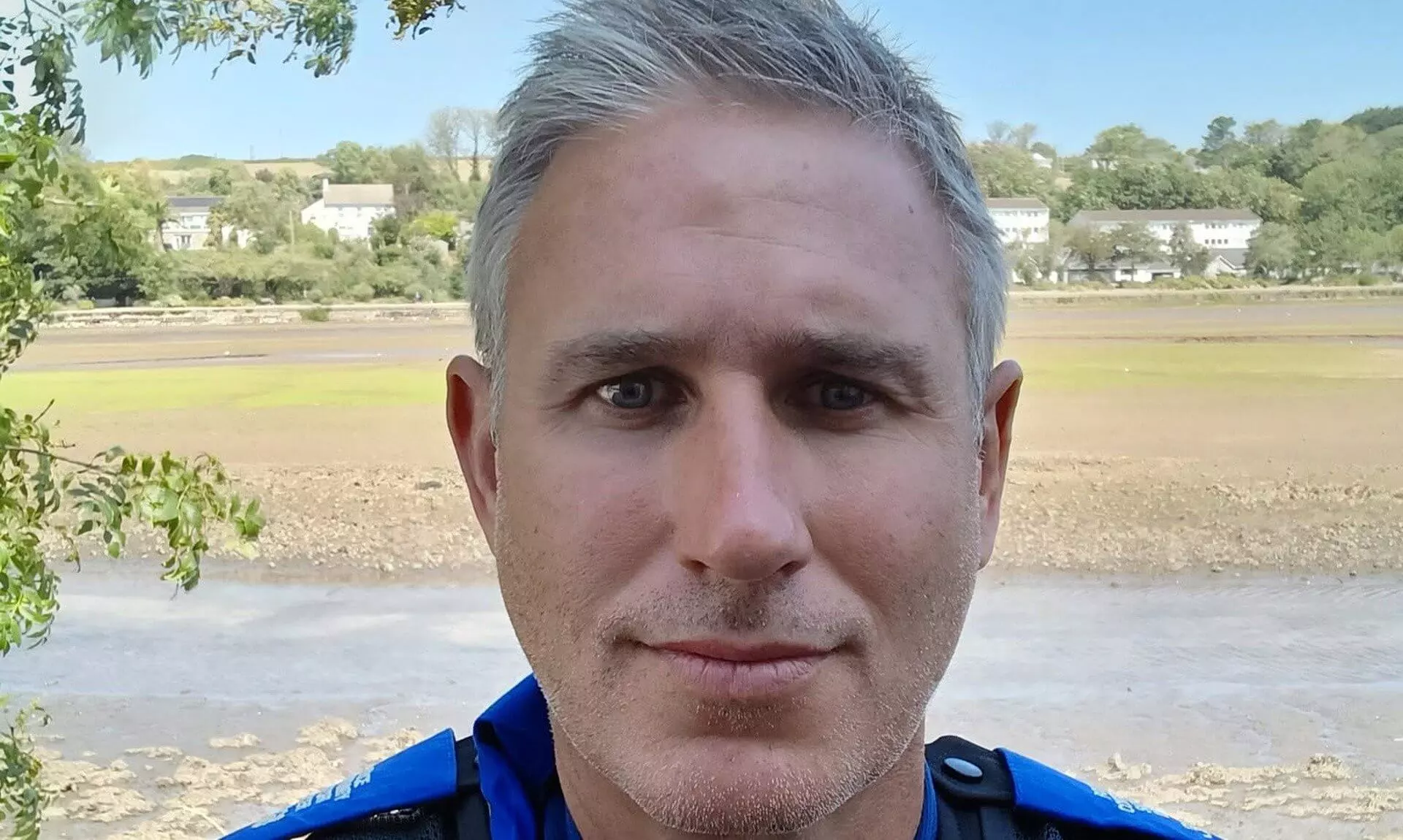 PCSO Aidan Jepson in uniform with mudflats and houses behind him