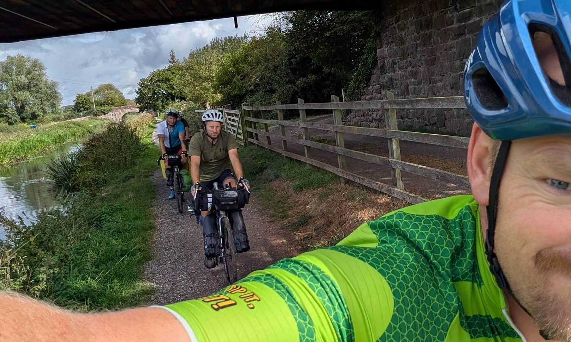 The four riders cycling a canal towpath under a bridge on the way to Land's End