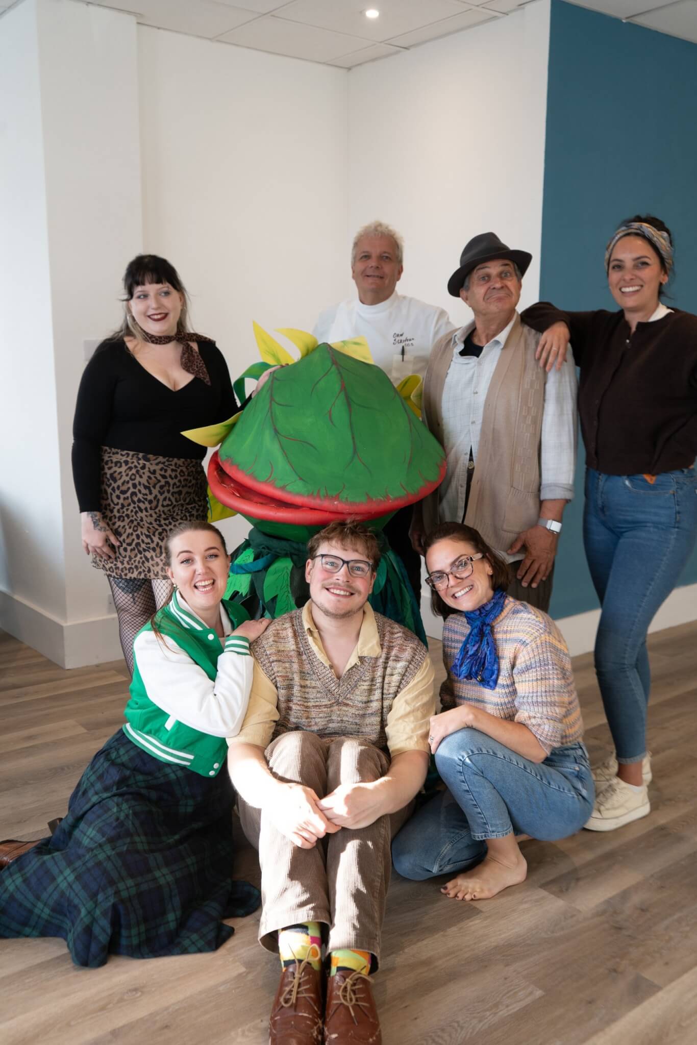 The Little Shop of Horrors cast smiling around the Audrey II puppet