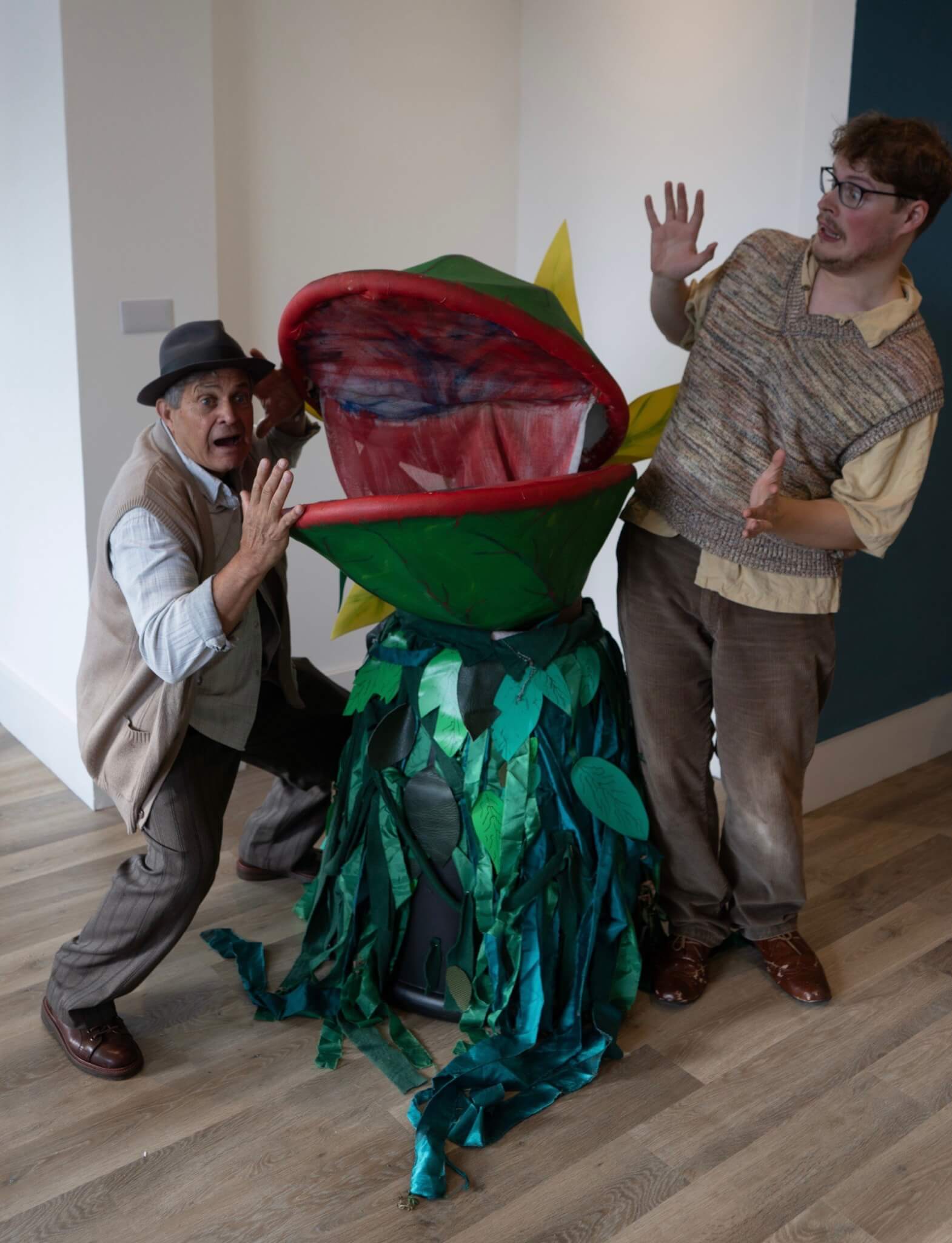 The Audrey II puppet opens its mouth wide as two cast members back away