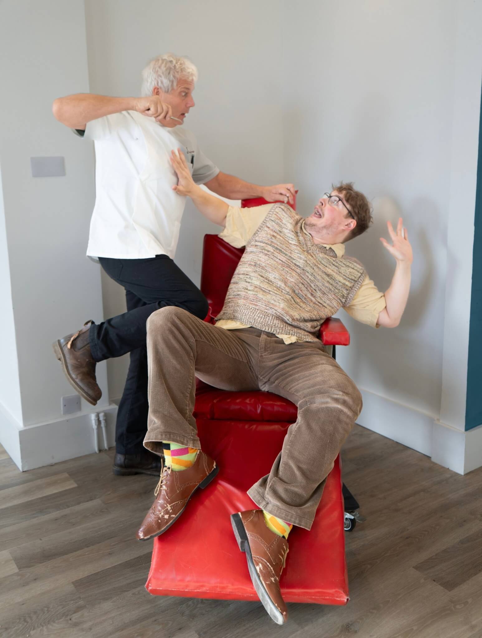 A cast member in a dentist's coat looms over a terrified man in a red chair