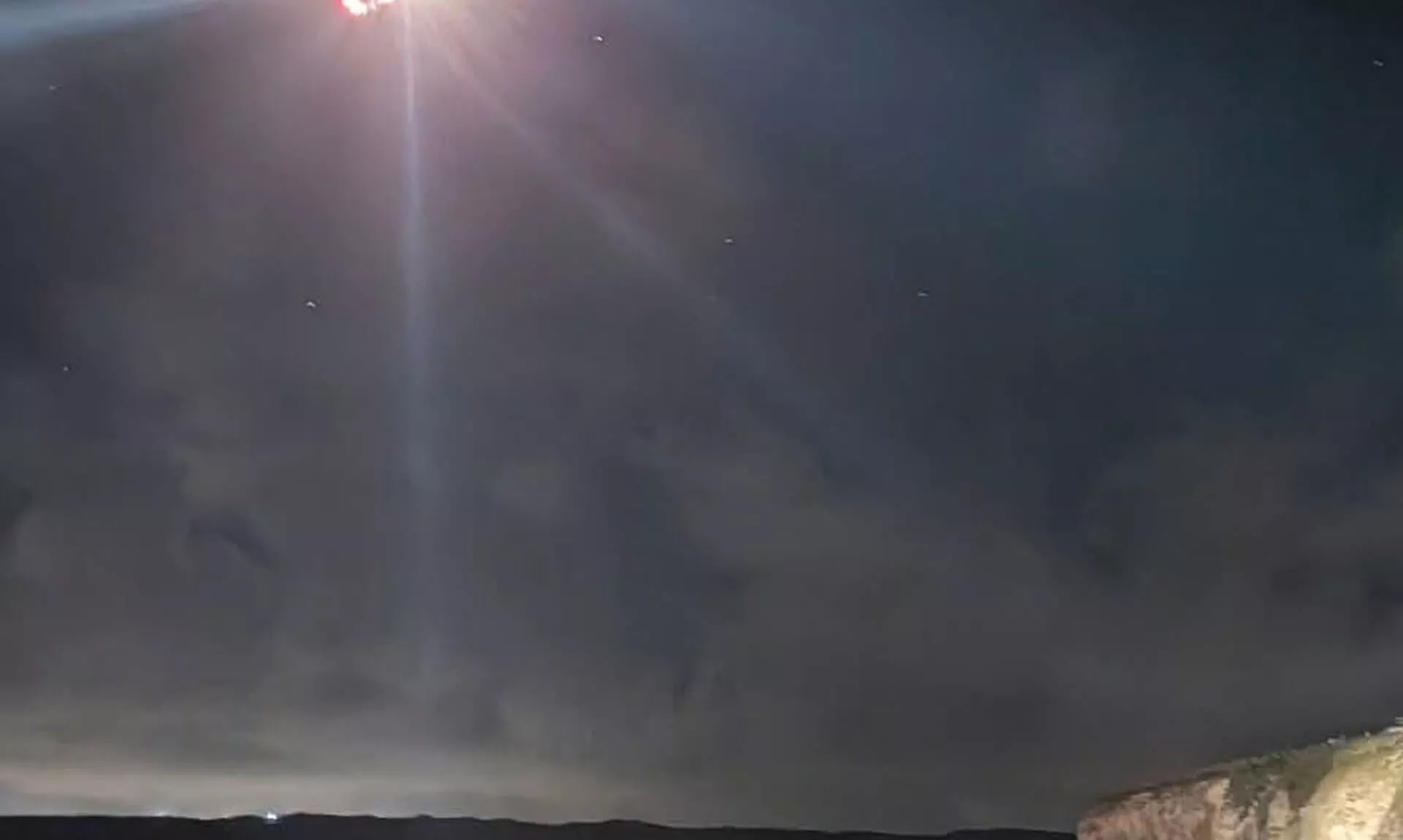 A rescuer's headtorch beam cuts through the night sky above the cliffs and sea at Perranporth