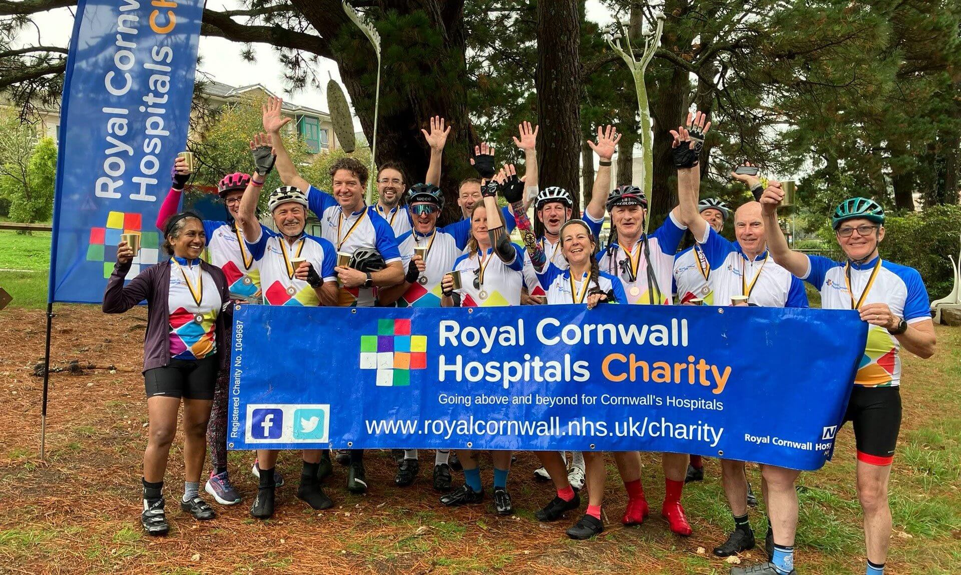Pedal 4 Patients cyclists celebrating behind a Royal Cornwall Hospitals Charity banner