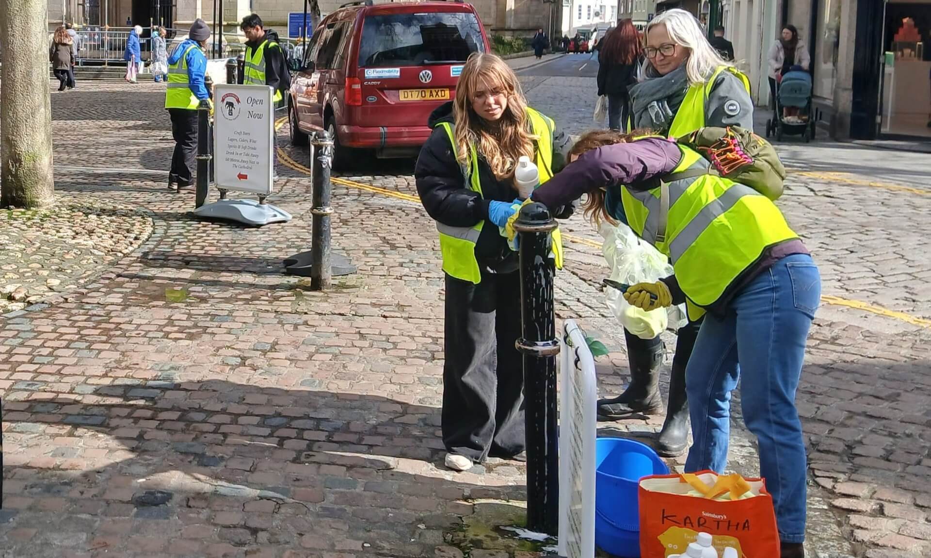 Volunteers in hi-vis vests cleaning a lamp post in Truro city centre