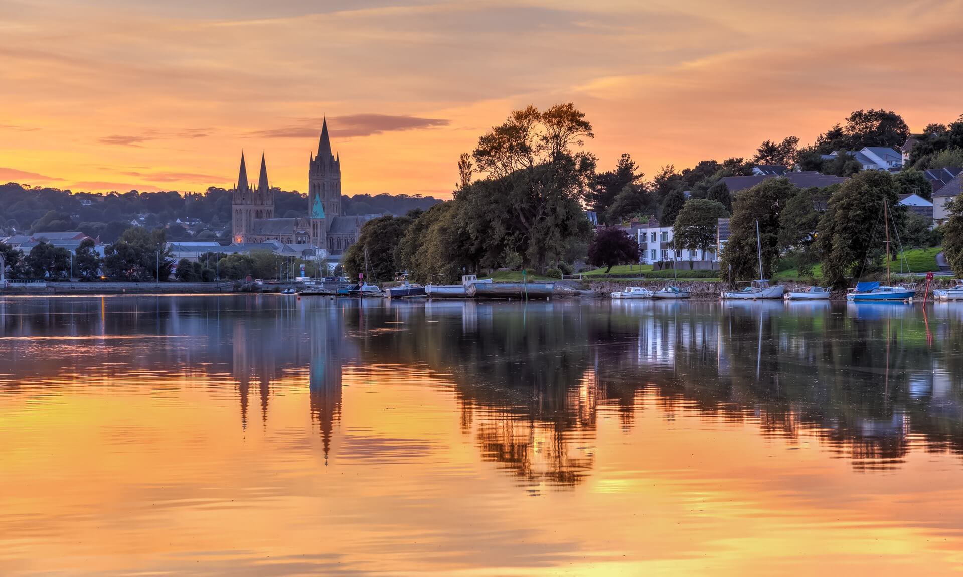 Truro Cathedral and the river at sunset with boats moored along the bank