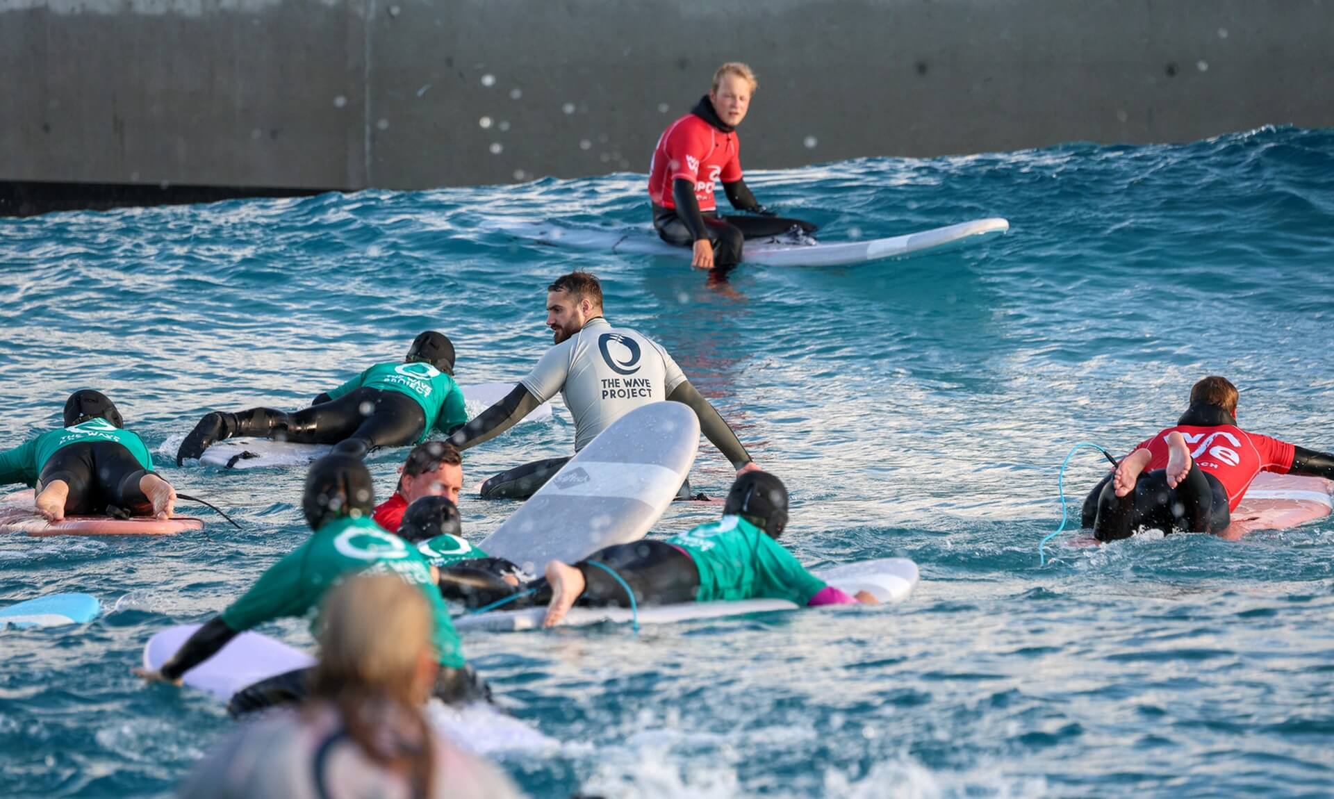 Young people paddling out with Wave Project mentors at an inland wave pool