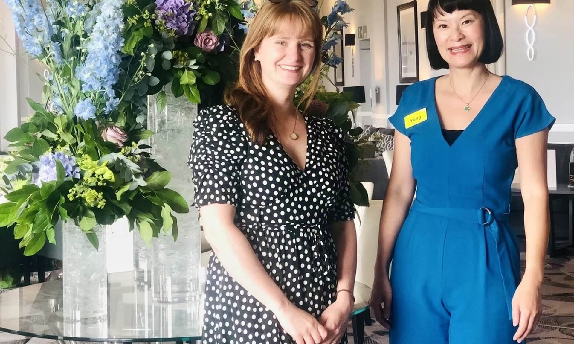 Pharmacist Yung Strawbridge standing with Abigail Wilson beside a large flower display