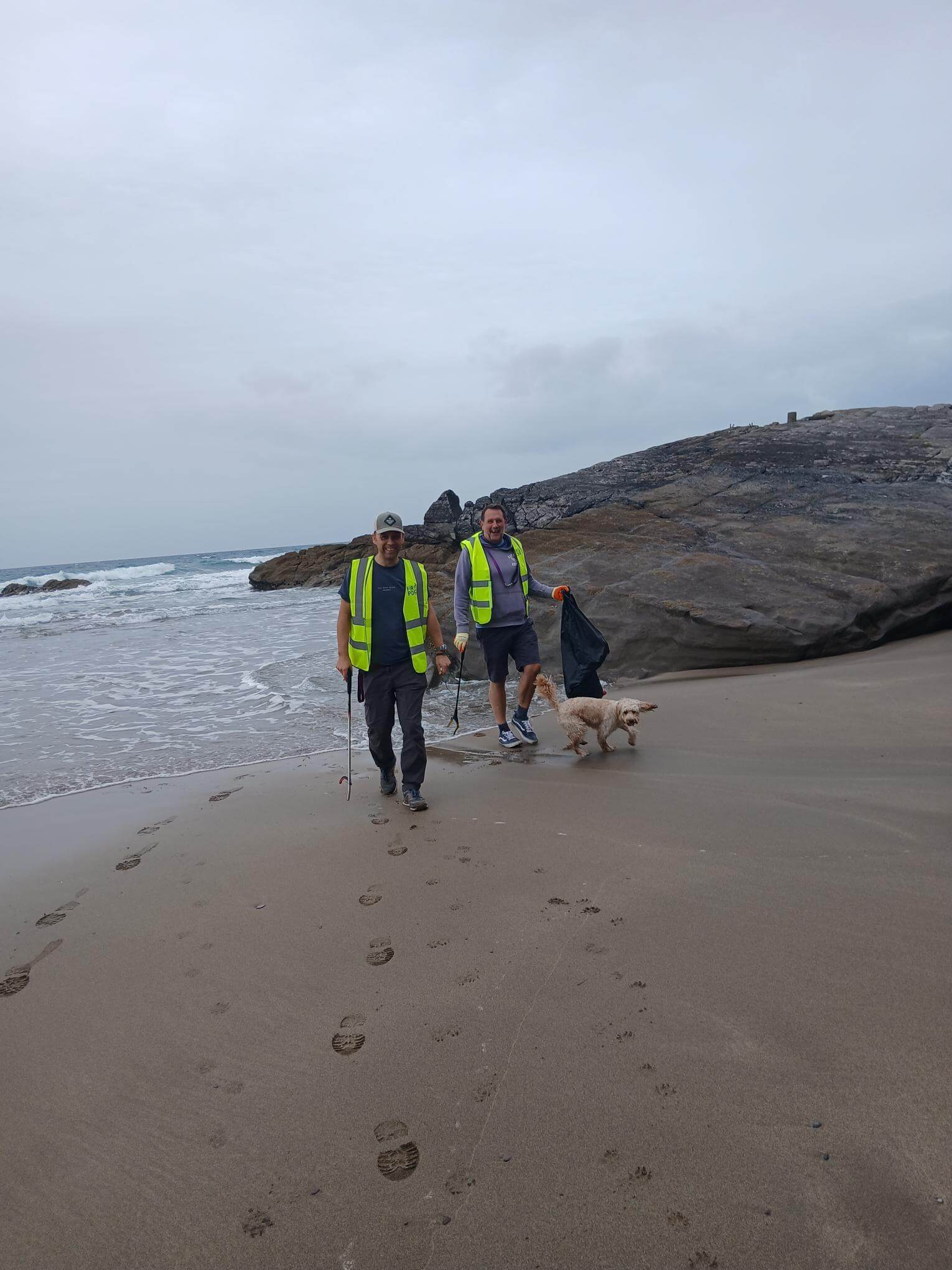 Two beach clean volunteers in hi-vis vests with a dog at Tregonhawke Beach