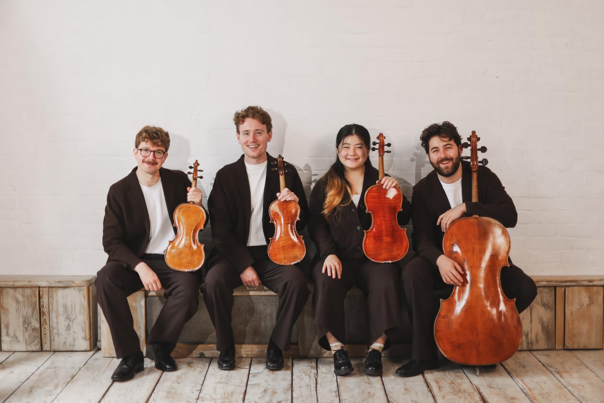 The Elmore Quartet sitting on a bench holding their violins, viola and cello
