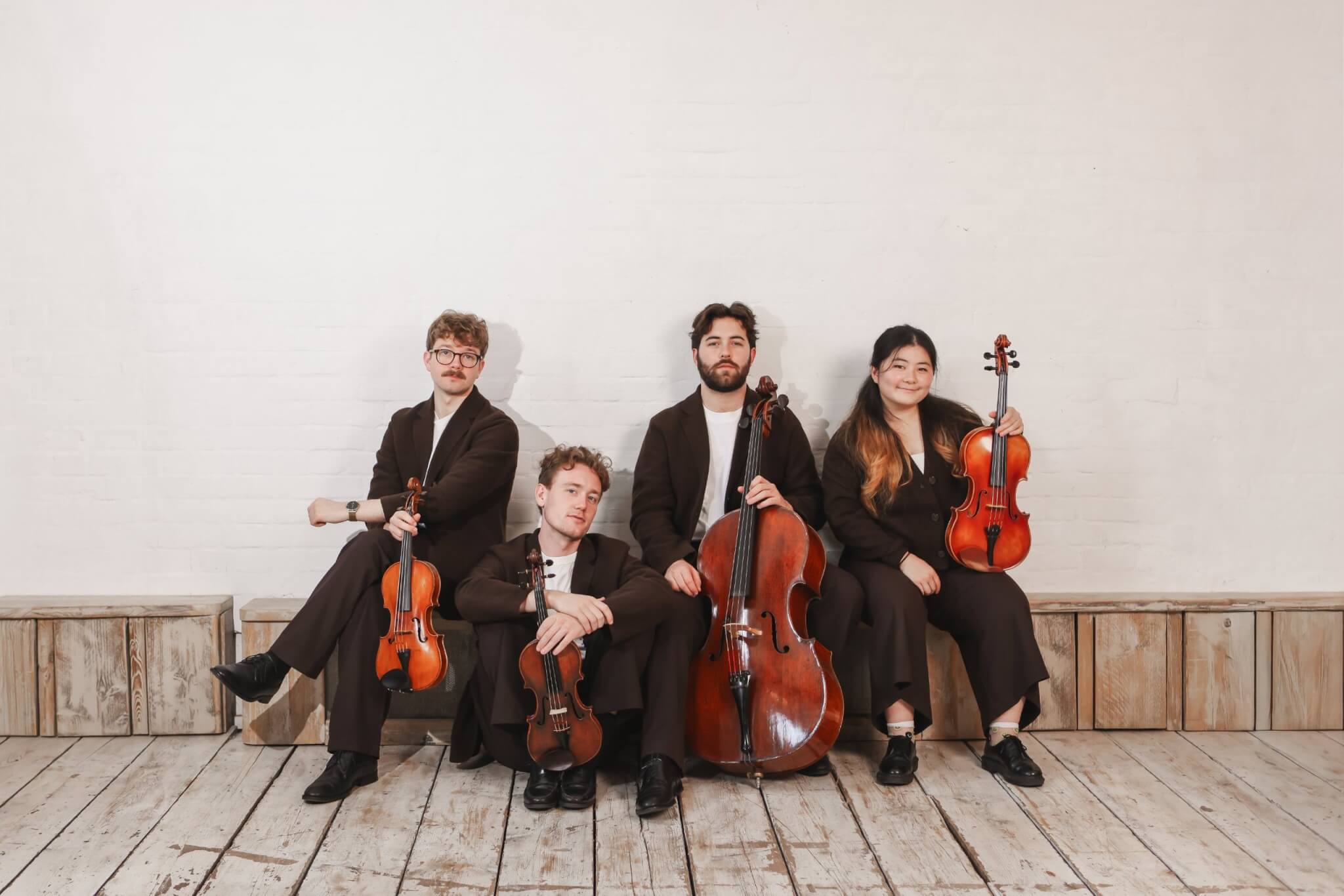 The Elmore Quartet with their instruments against a white brick wall