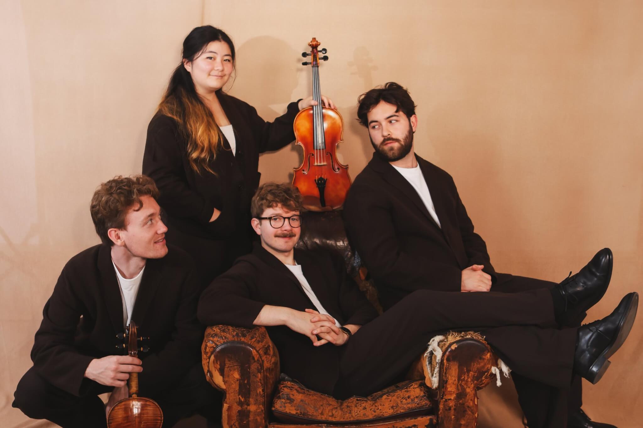 The Elmore Quartet posing around a worn leather armchair
