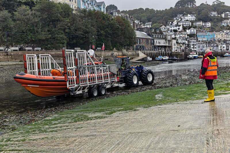 Looe RNLI inshore lifeboat on its launch trailer behind a tractor on the river bed at low tide