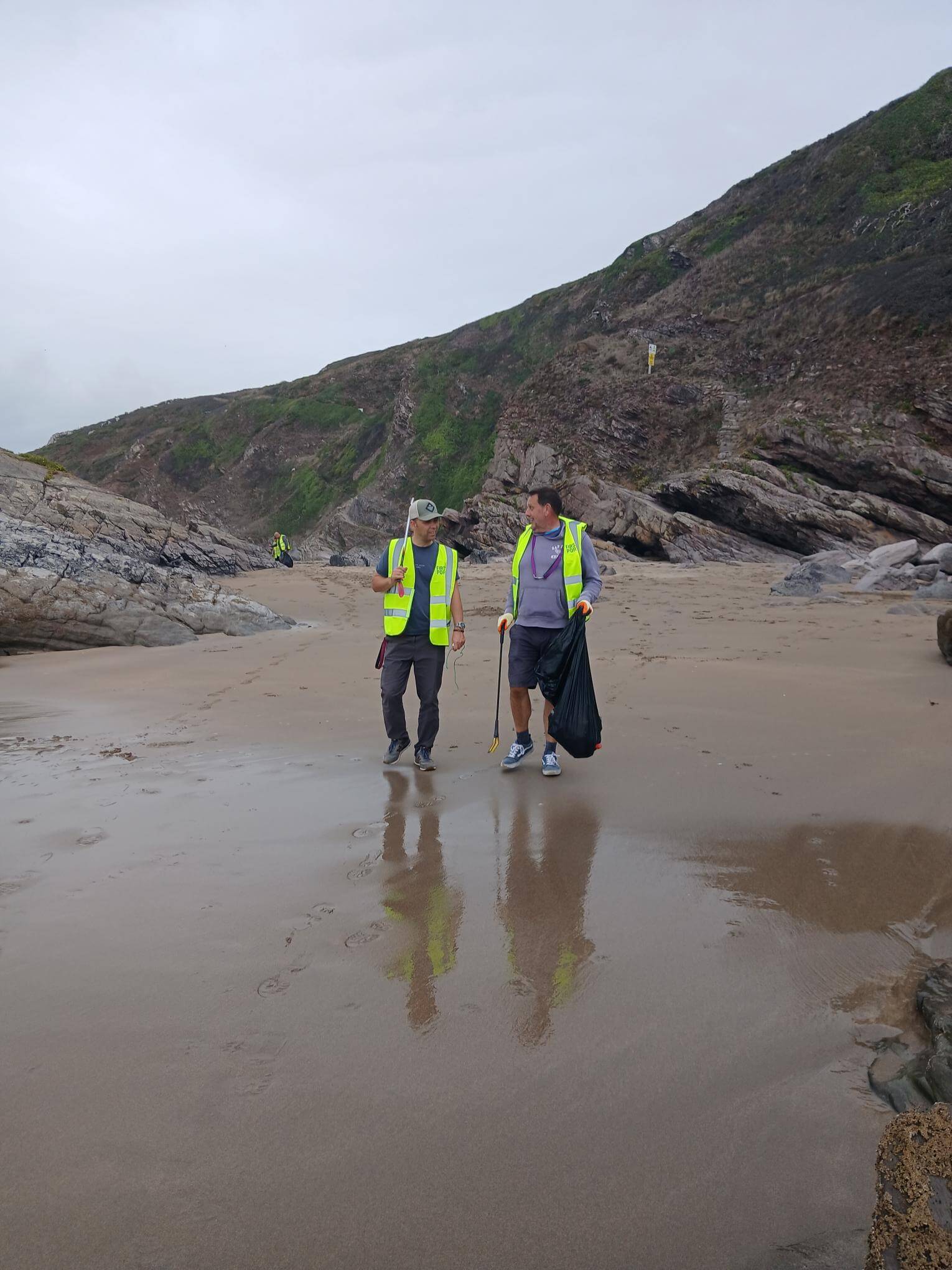 Two volunteers with litter pickers and a bin bag walking across Tregonhawke Beach