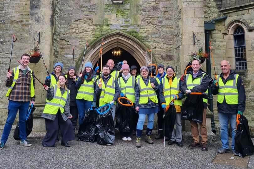Volunteers in high-vis vests holding litter pickers and black bags outside a stone building in Truro