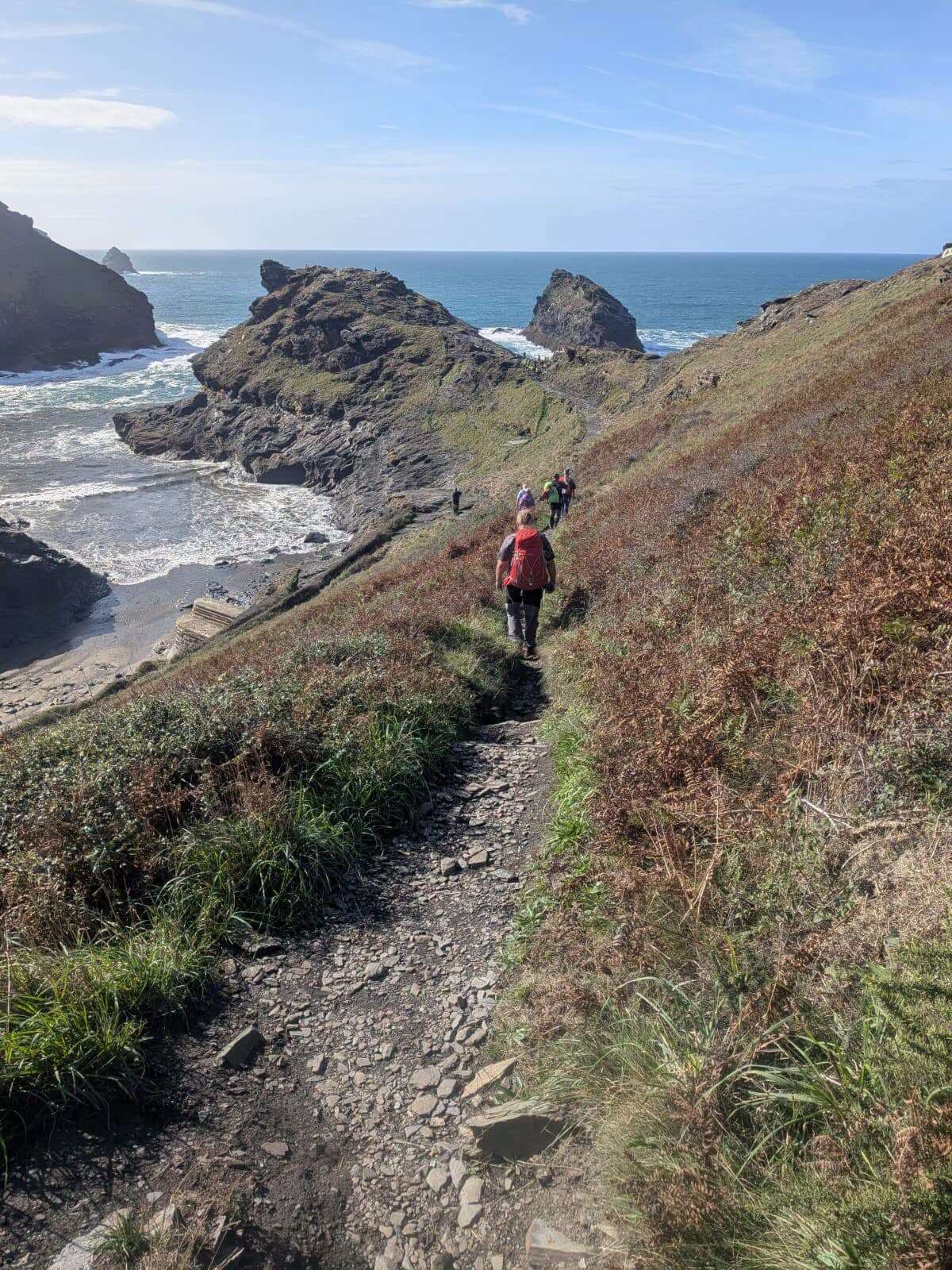 Search volunteers walking in single file down a stony coast path towards the sea