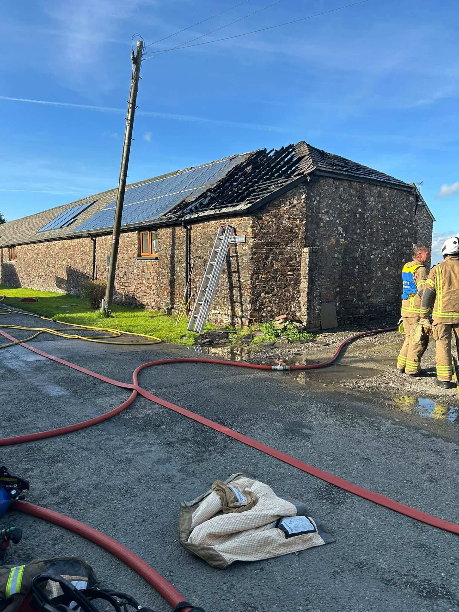 Stone barn conversion near Week St Mary with fire-damaged roof and fire hoses across the road