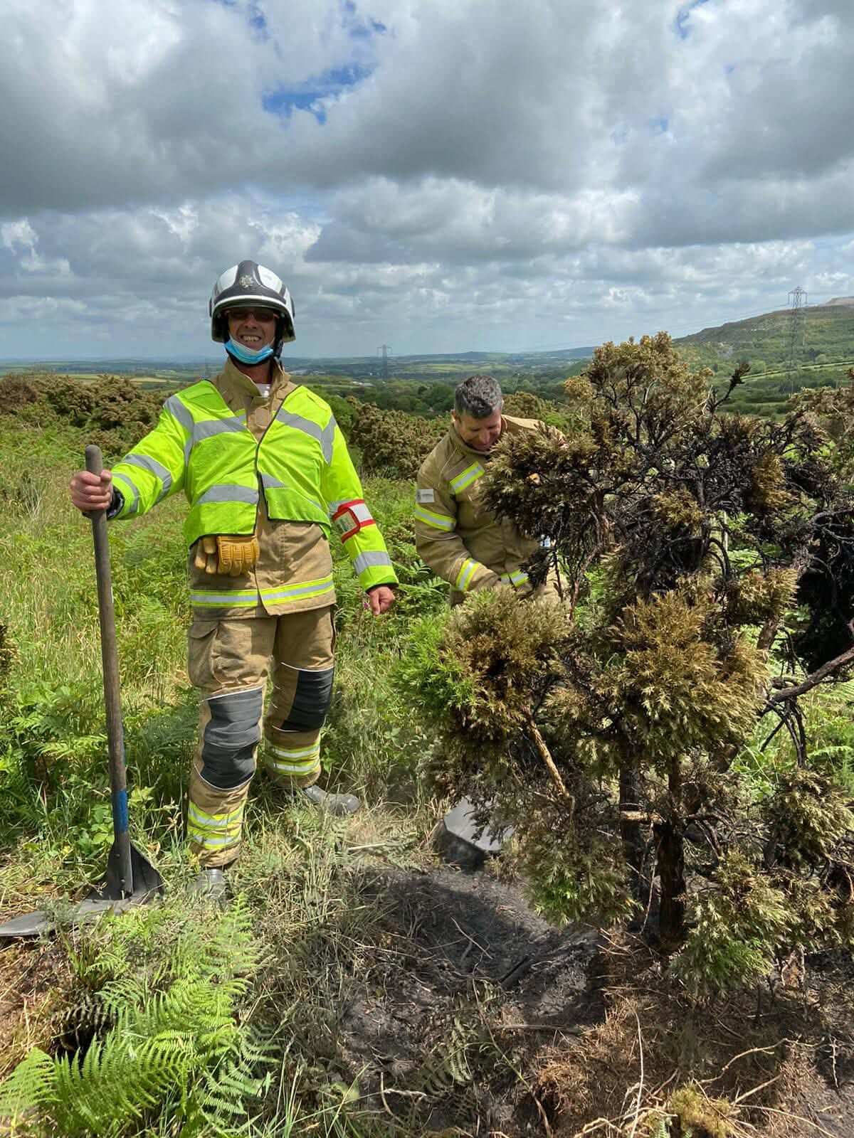 Two firefighters working among burnt gorse on open ground