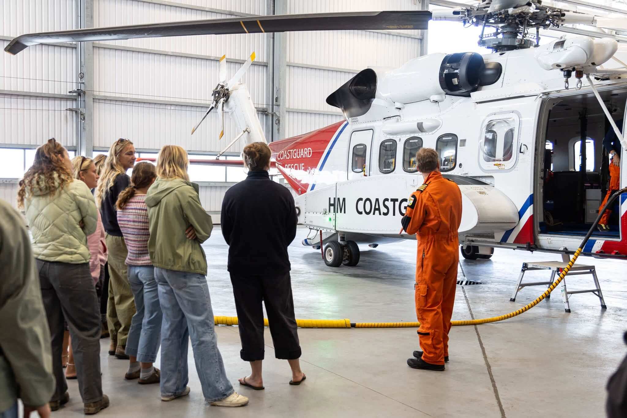 A group looking at an HM Coastguard rescue helicopter in a hangar