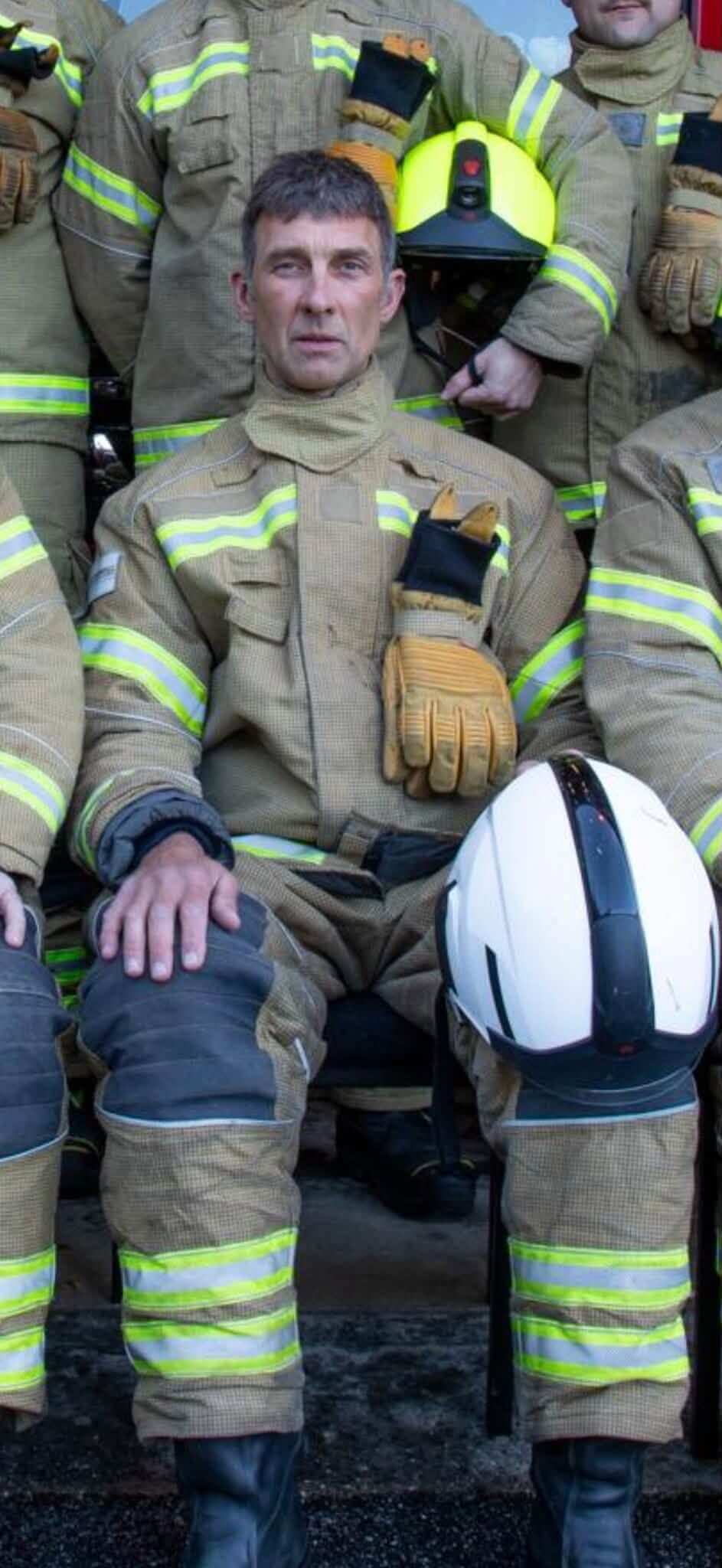 Firefighter in kit seated among crew, holding a white helmet