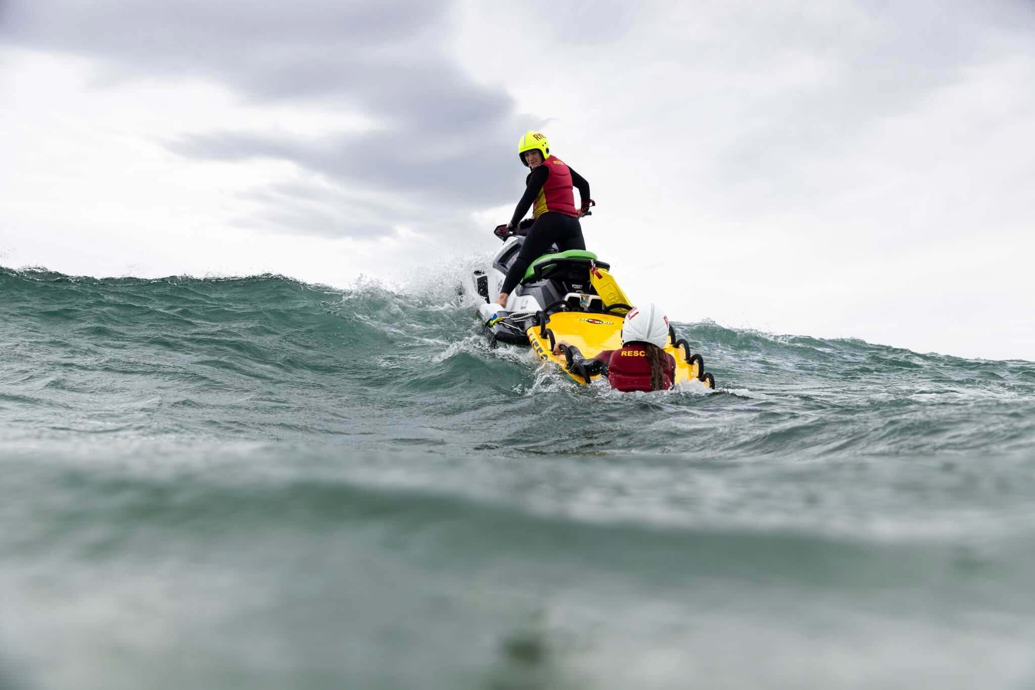 A lifeguard on a rescue watercraft towing a rescue sled with a second lifeguard