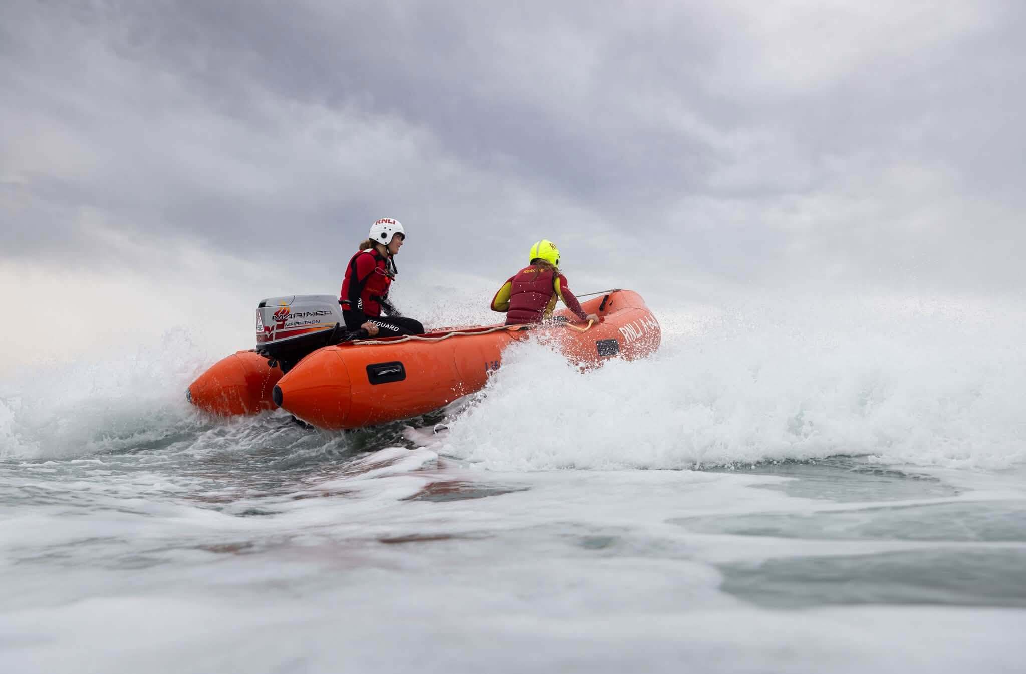 Two lifeguards in an orange inshore rescue boat going through surf